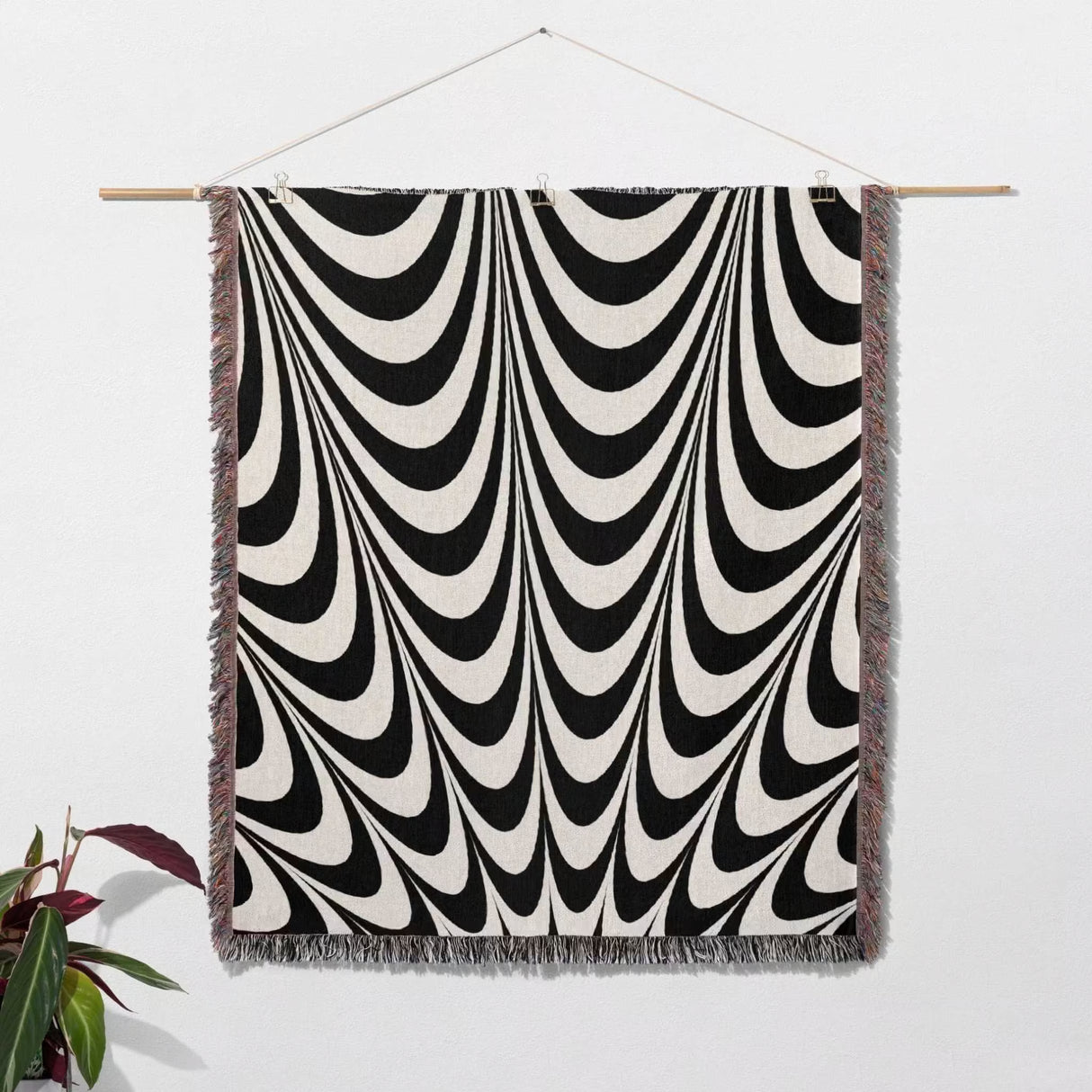 Black and white abstract art wavy woven blanket throw tapestry with multicolor fringe hanging on a wooden rod against a white wall.