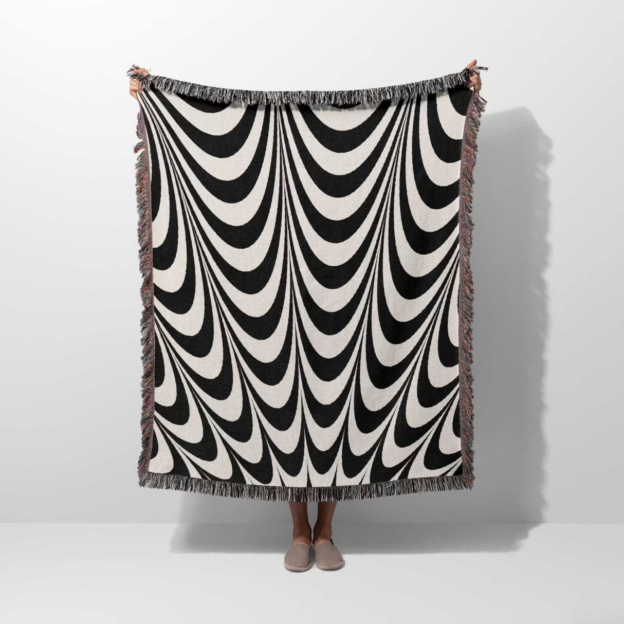 Black and white abstract art wavy woven blanket throw tapestry hold by a person on a white background.