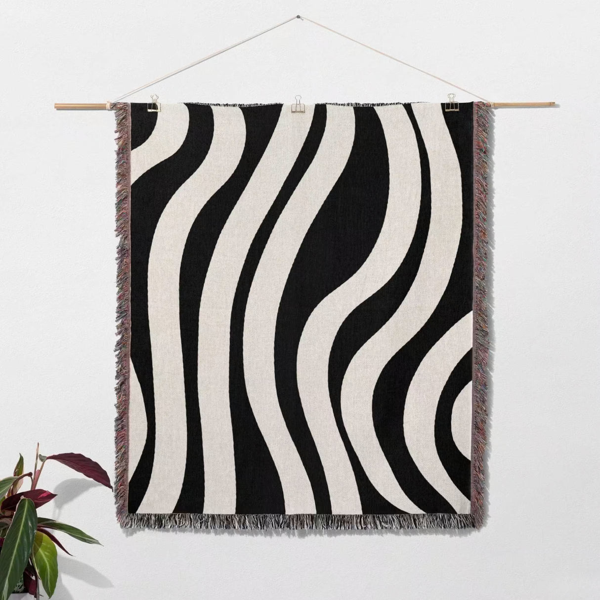 Black and white abstract shapes woven blanket throw tapestry hanging on a wooden rod against a white wall.