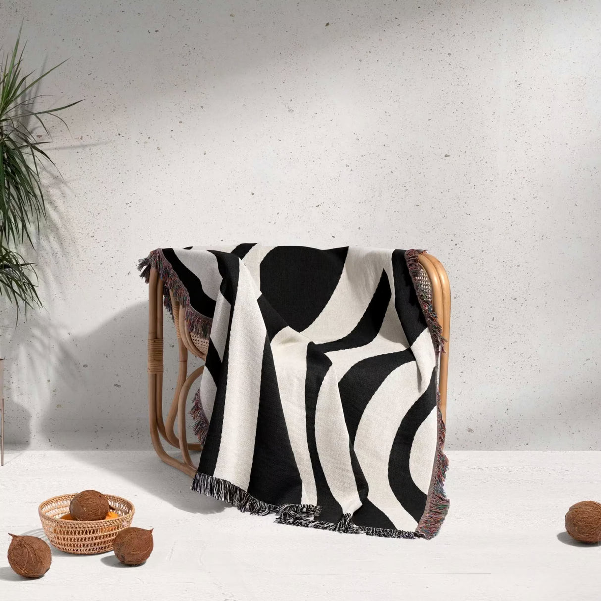 Black and white abstract shapes woven blanket throw tapestry draped over a chair against a light gray wall.