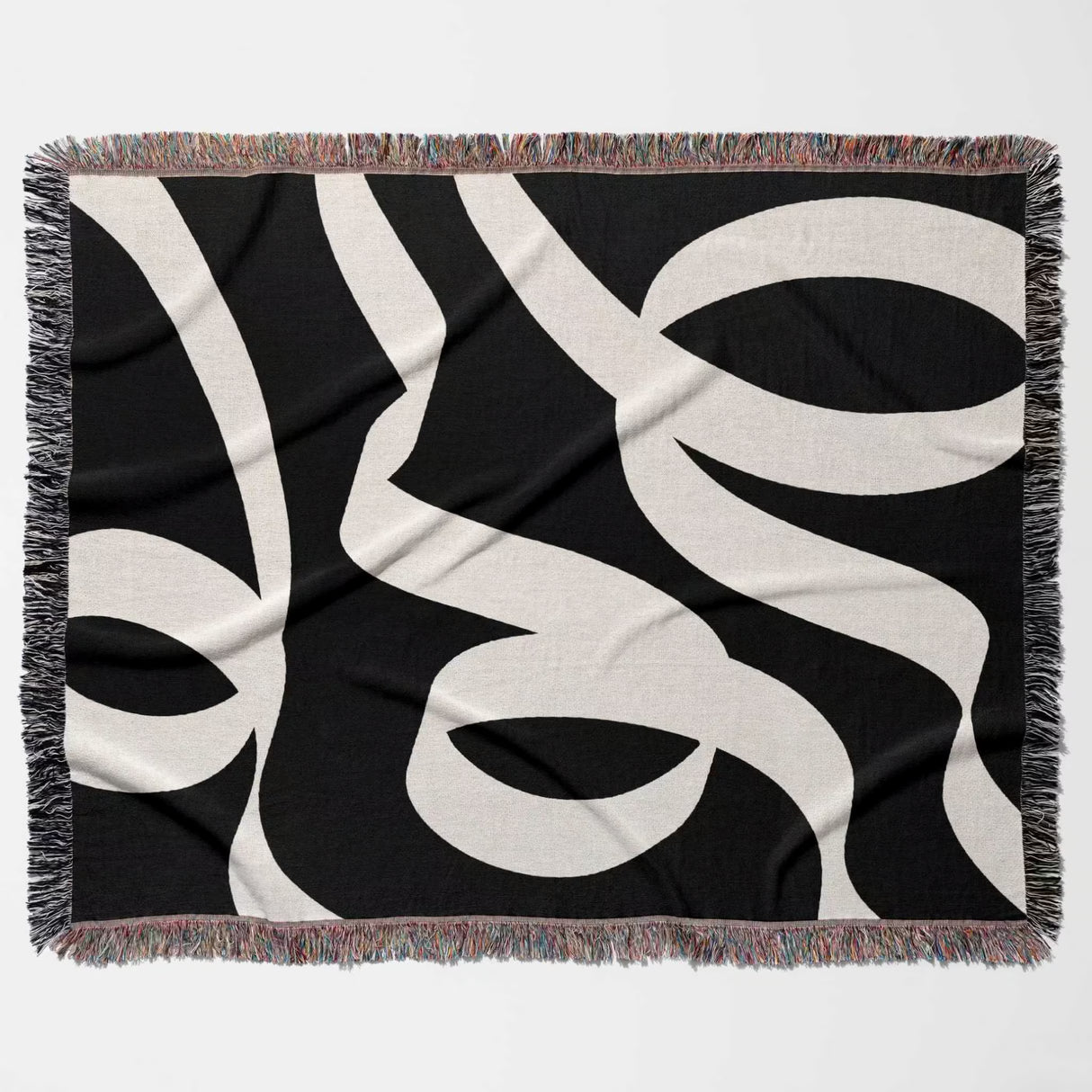 Black and white abstract waves accent woven blanket throw with fringe flat lay on a white background.