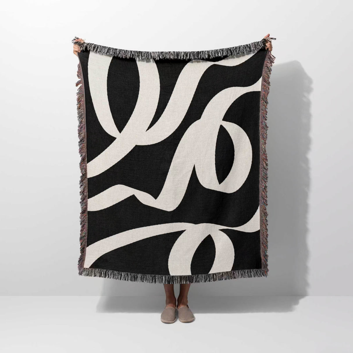 Black and white abstract waves accent woven blanket throw draped over a person on a white background