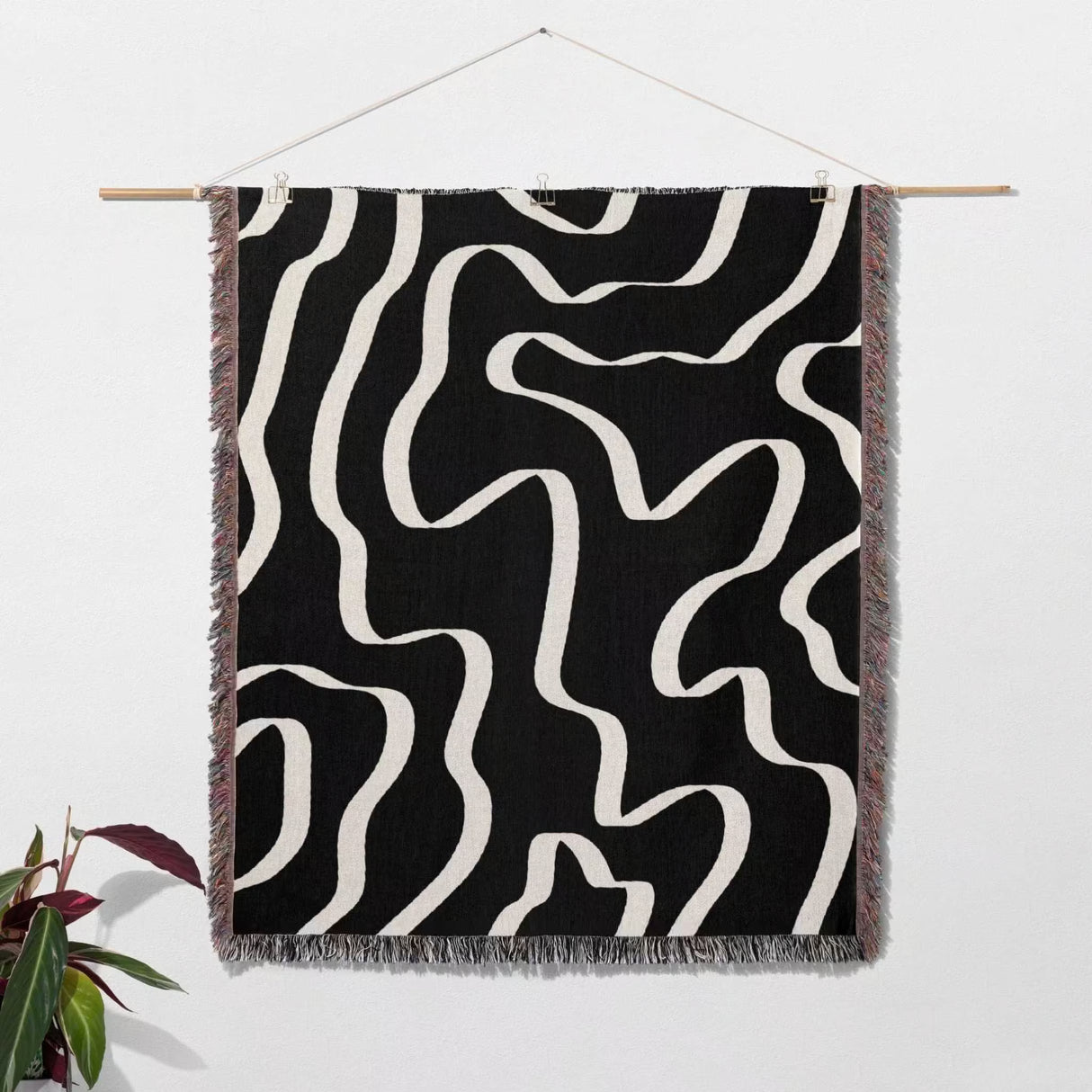 Black and white abstract waves artistic woven blanket throw with fringe hanging on a wooden rod against a white wall.