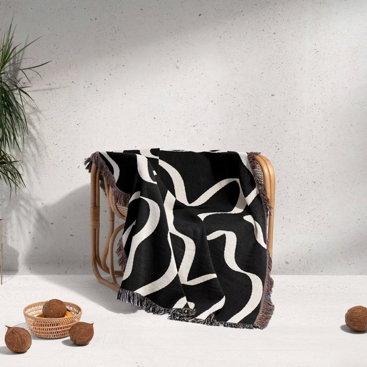 Black and white abstract waves artistic woven blanket throw draped over a chair against a light gray wall.