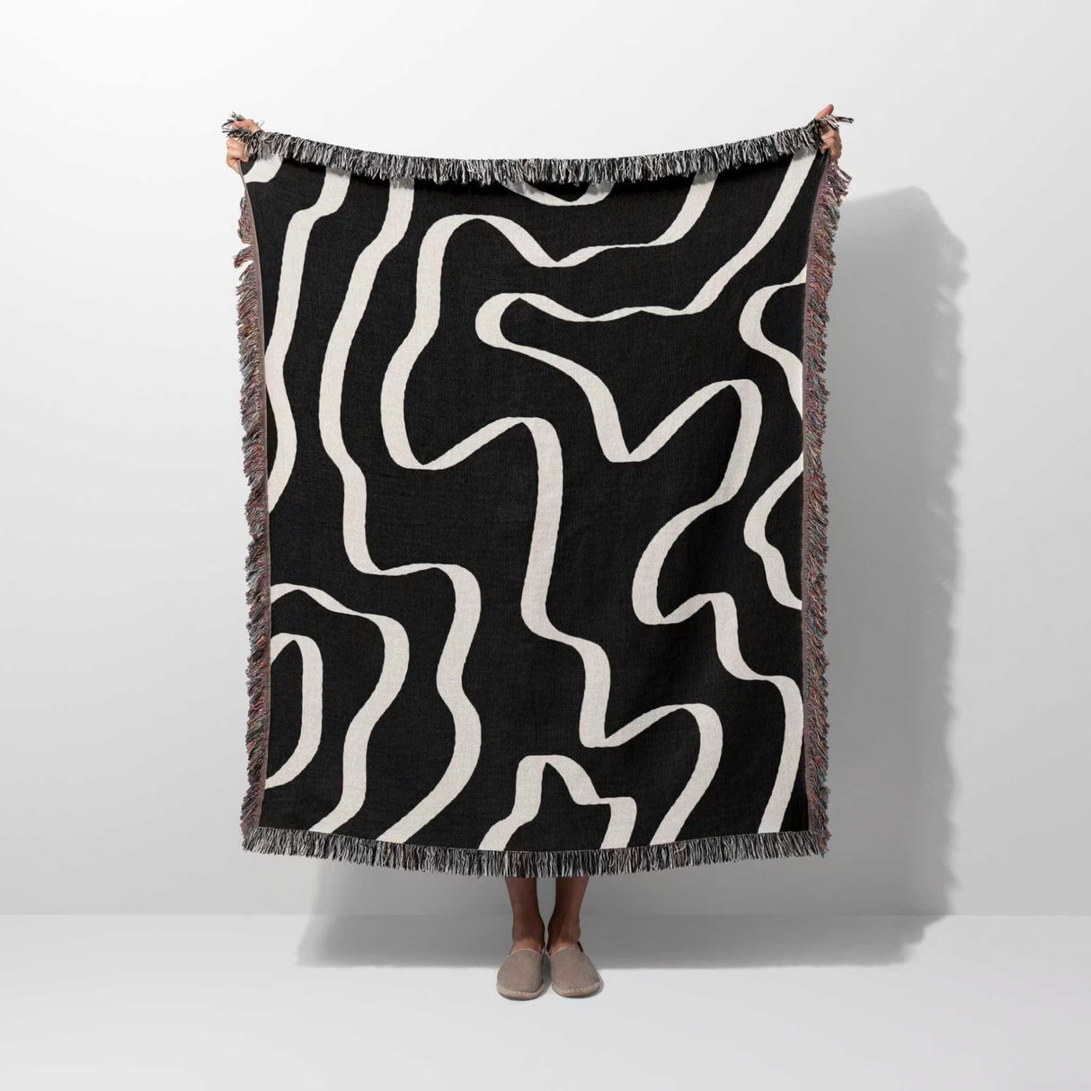 Person holding a black and white abstract waves artistic woven blanket throw against a white background