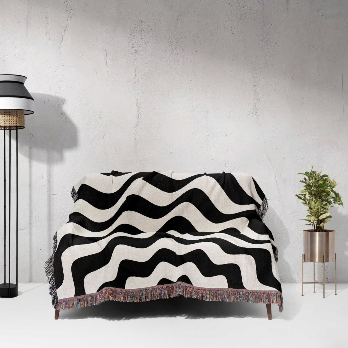 Black and white abstract wavey lines woven blanket throw tapestry draped over a sofa against a light gray wall.