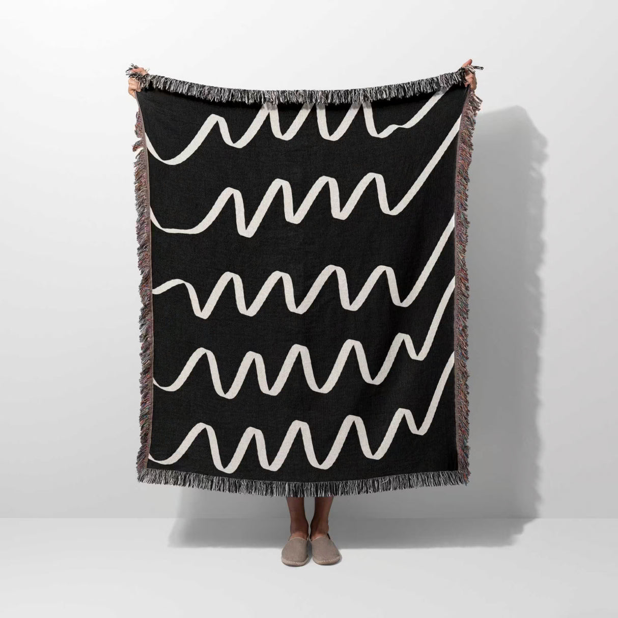 Black and white accent decorative woven blanket throw tapestry with wavy lines held by a person on a white background