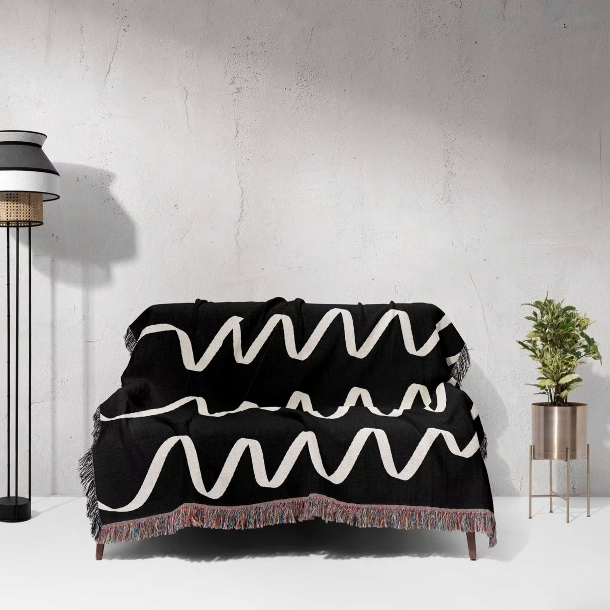 Black and white accent decorative woven blanket throw tapestry with zigzag pattern draped over a couch against a white wall.