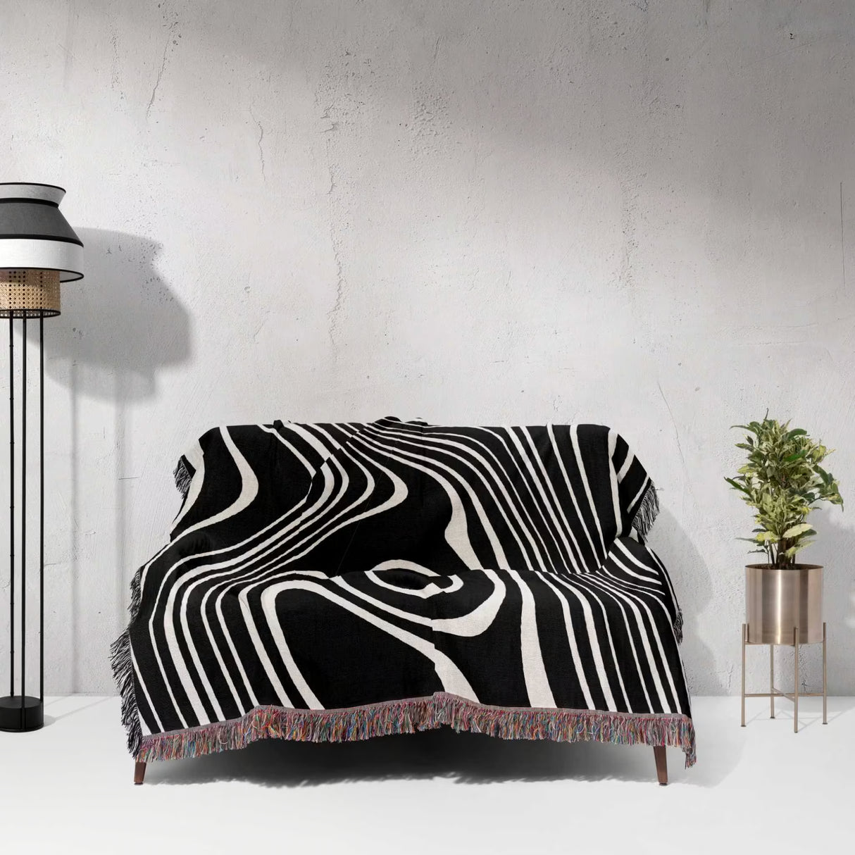 Black and white abstract woven throw blanket draped over a sofa against a white wall.