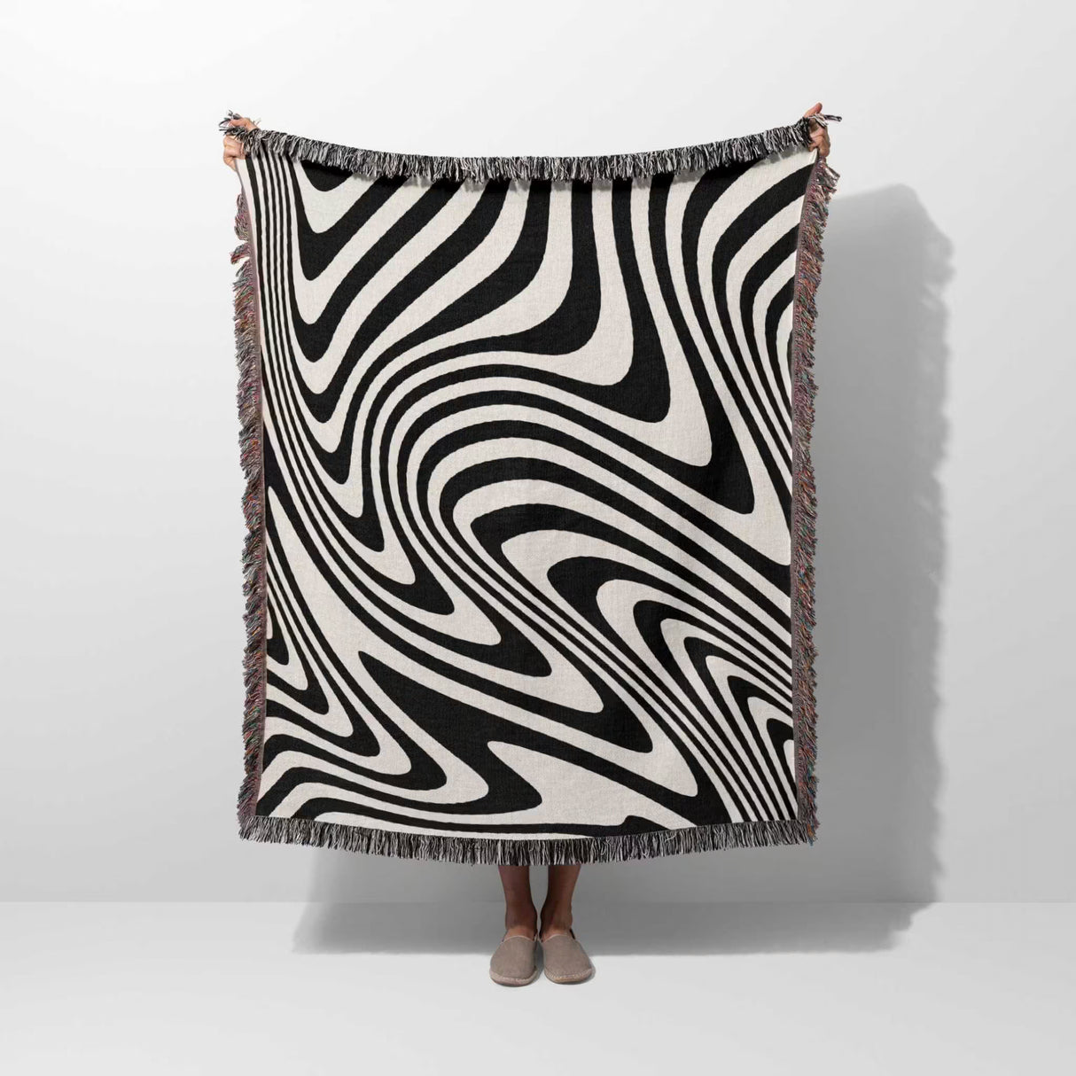 Person holding a black and white modern decorative woven throw blanket against a white background