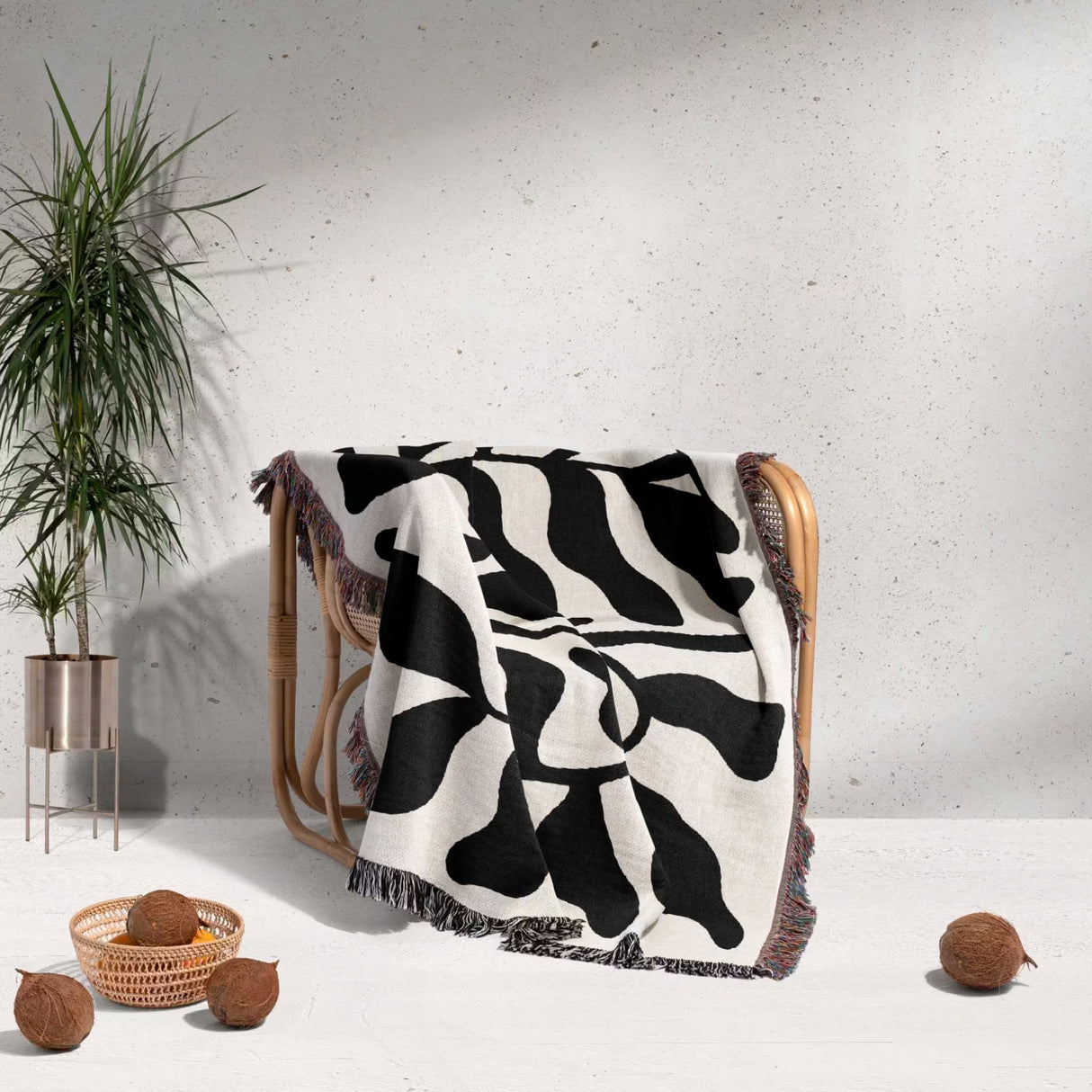 Black leaf Matisse throw blanket draped over a chair with a plant and coconuts in the background.