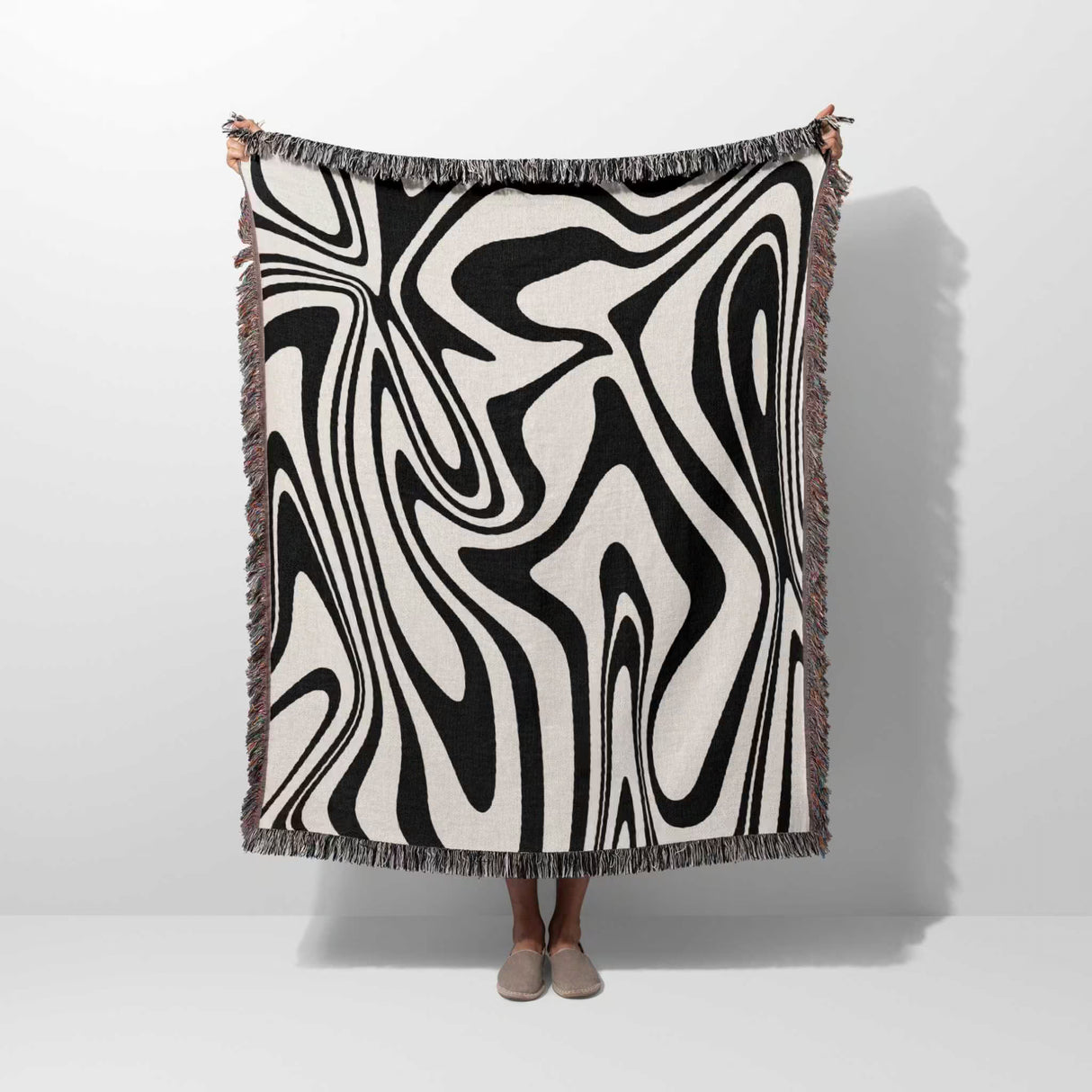 Person holding a black and white marble woven throw blanket against a white background