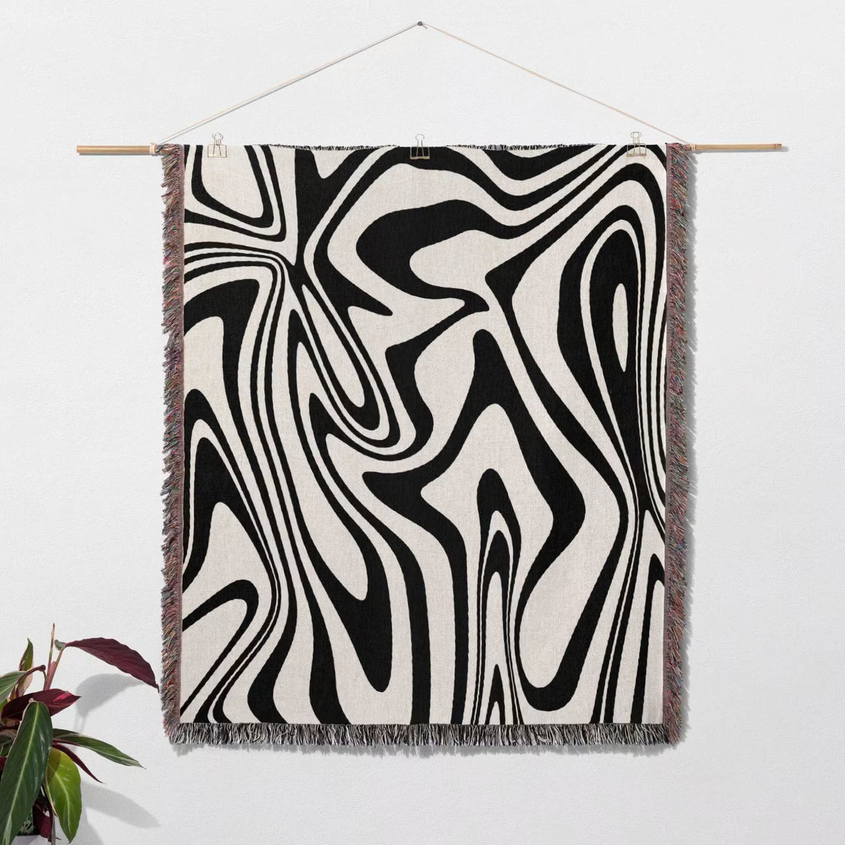 Black and white marble woven throw blanket tapestry hanging on a white wall with a plant in the corner.