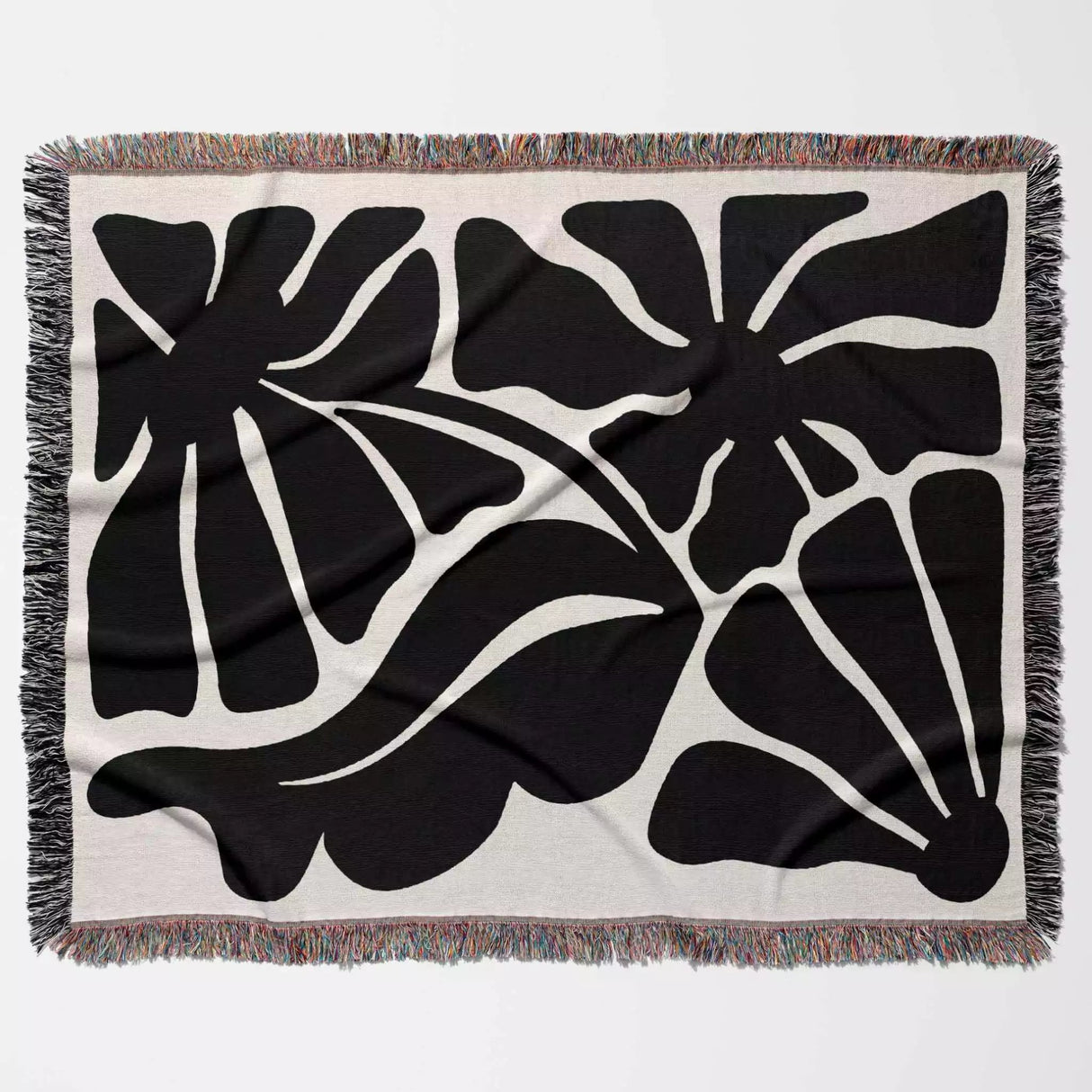 Abstract leaf black and white Matisse flowers woven throw blanket on a beige background with fringe edges.