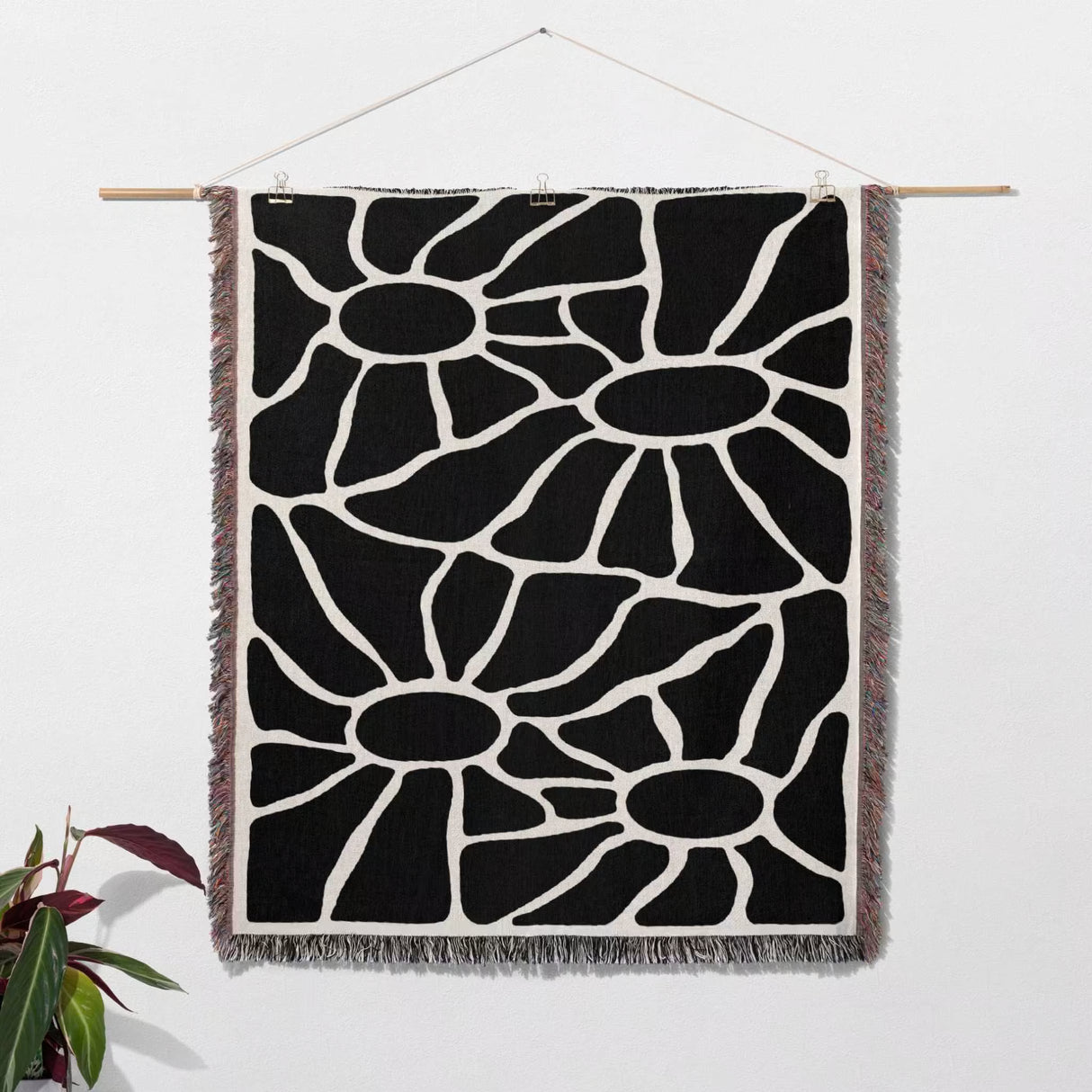 Black and white Matisse tapestry throw blanket for couch hanging on a white wall with a plant in the corner.