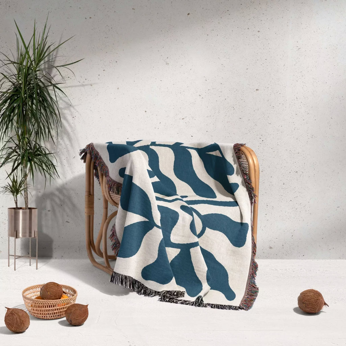 Blue leaf Matisse throw blanket draped over a chair against a white wall.