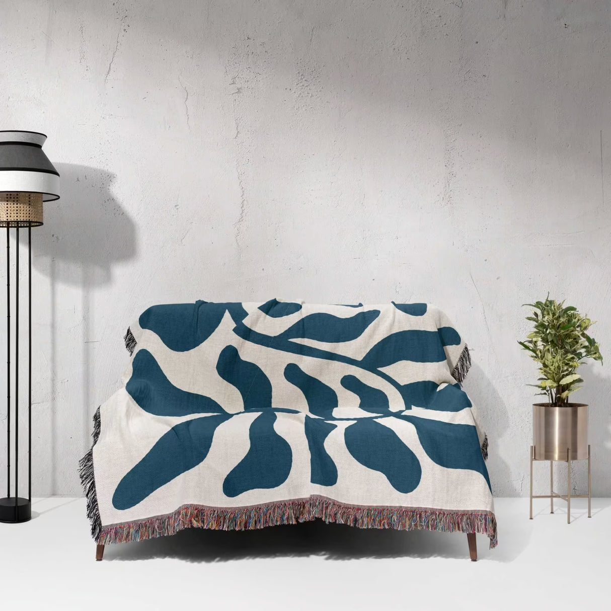Blue leaf Matisse throw blanket on a couch against a white wall.