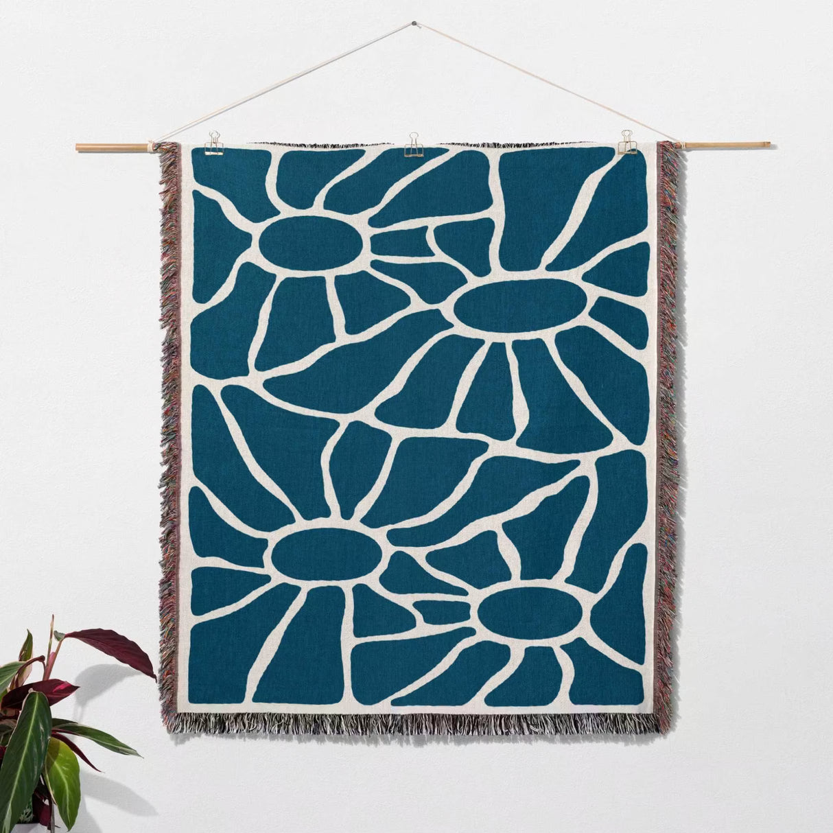 Blue Matisse tapestry throw blanket for couch and bed as a wall hanging on a white wall with a plant on the side.