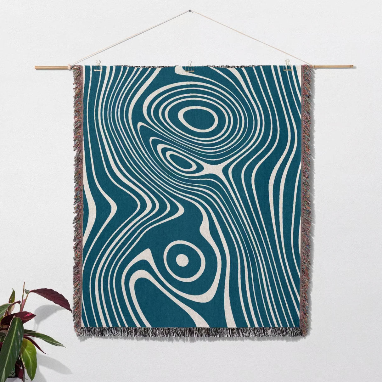 Blue trendy abstract woven throw blanket as woven wall art tapestry with a blue and white pattern on a white wall.