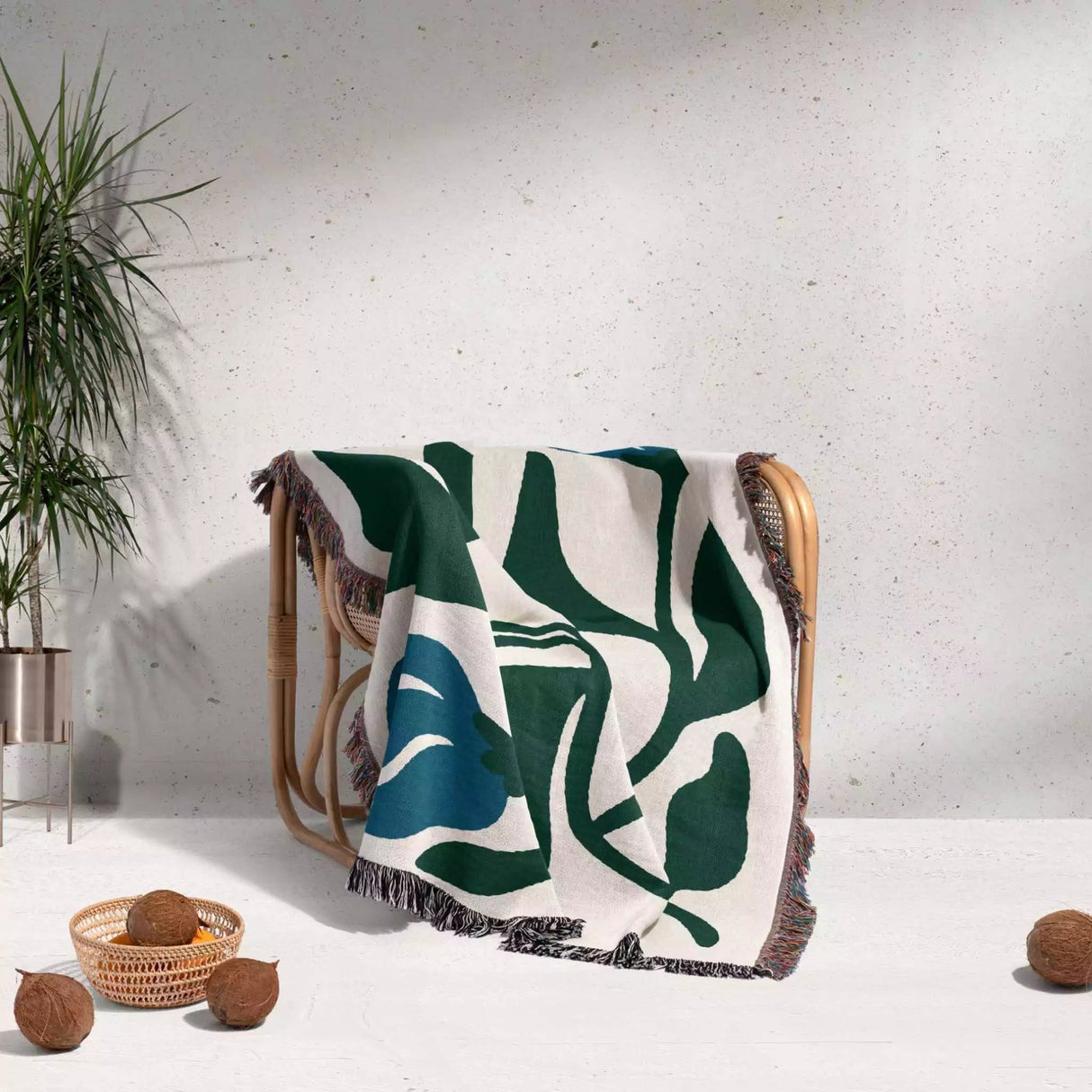 Decorative blue and green Matisse flower woven throw blanket with green leaf pattern draped over a chair against a white wall.
