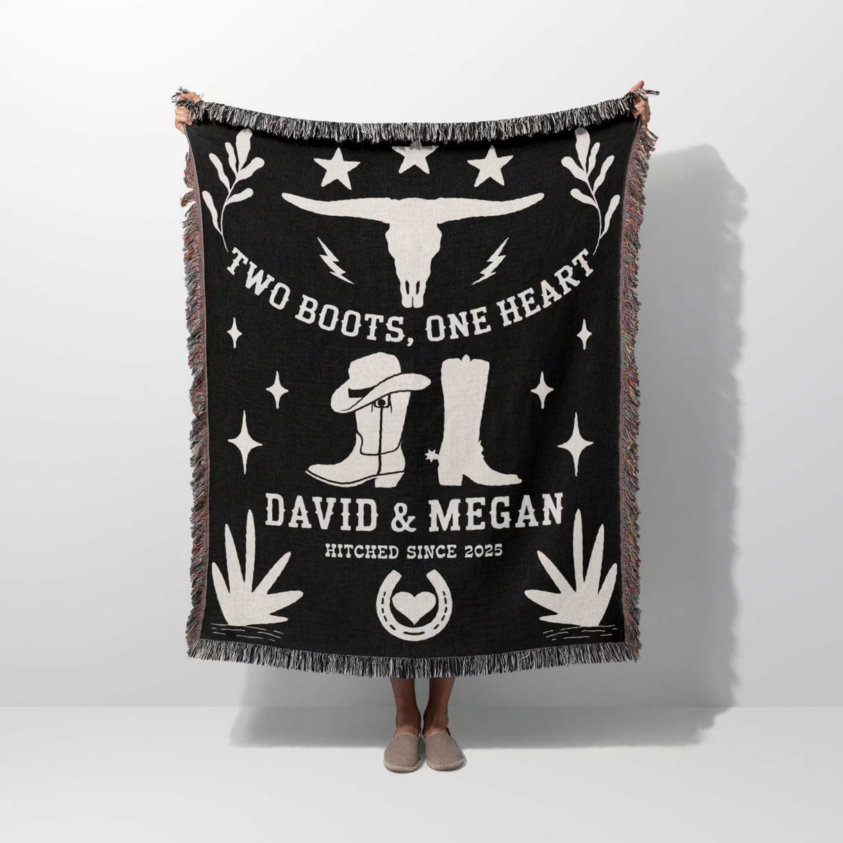 Cow skull and boots 2nd anniversary gift woven throw blanket with white text and graphics, including boots and a skull, held by a person on a white background.