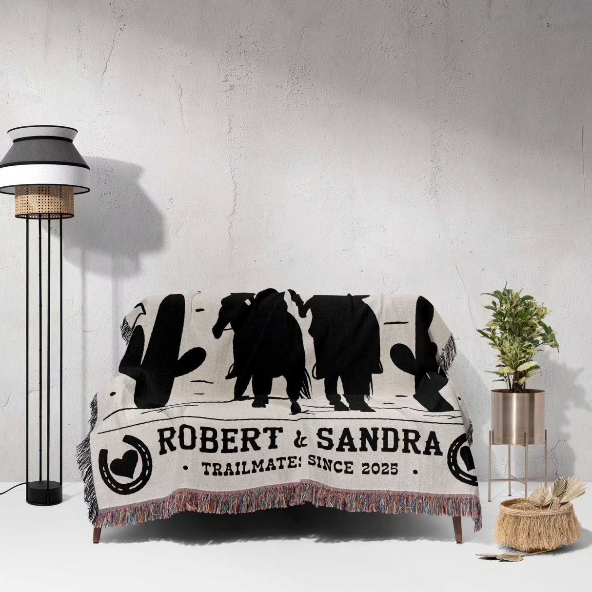 Cowboy and cowgirl cotton anniversary gift woven throw blanket with black animal silhouettes and text on a white couch against a light gray wall.