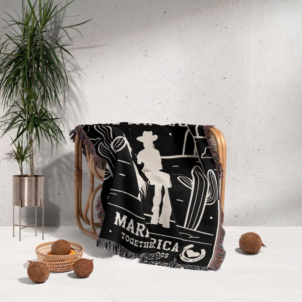 Cowboy and cowgirl couple 2nd anniversary gift woven throw blanket with western graphics and text draped over a chair, with a plant and decor items in the background.