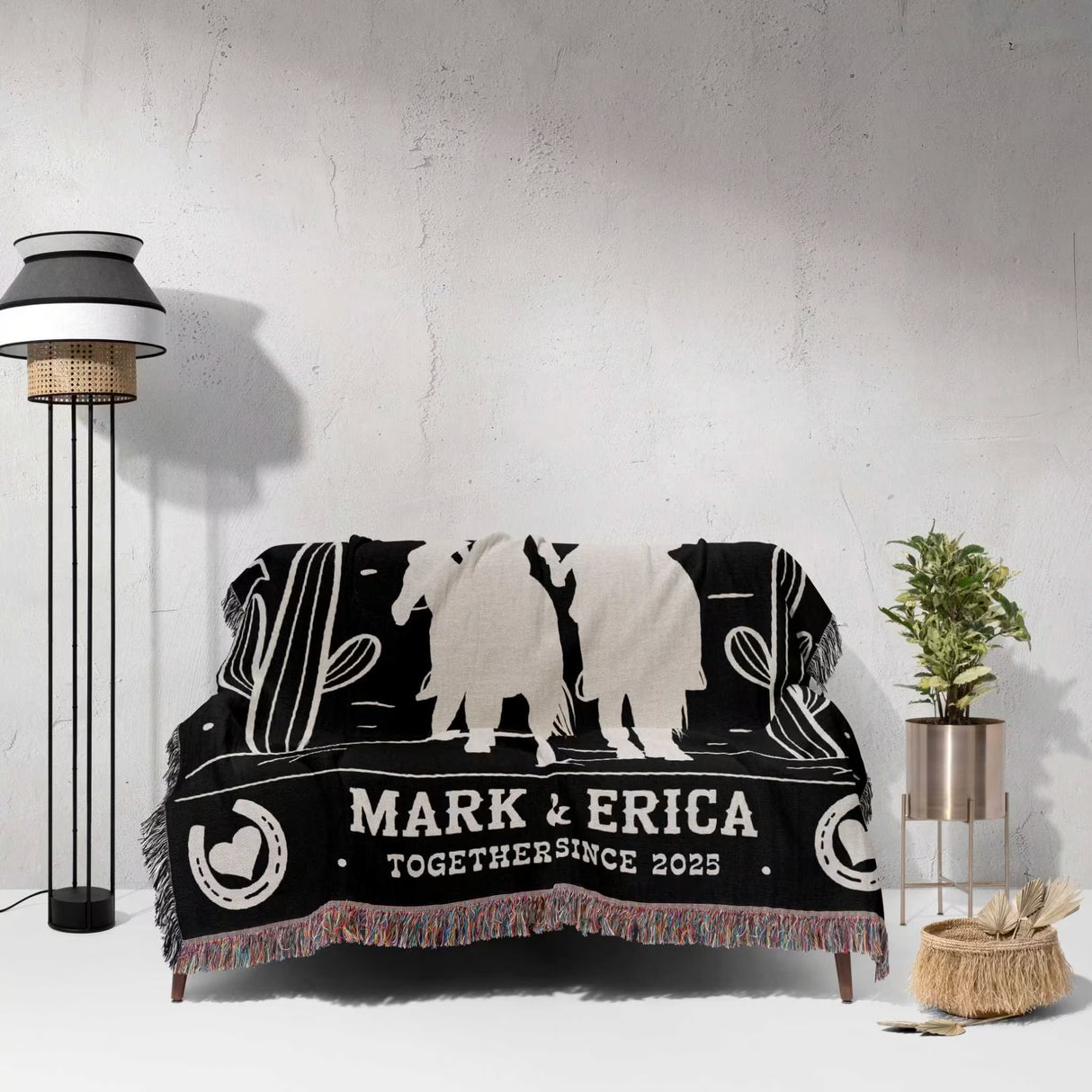 Cowboy and cowgirl couple 2nd anniversary gift woven throw blanket with western designs and text on a couch against a light gray wall.