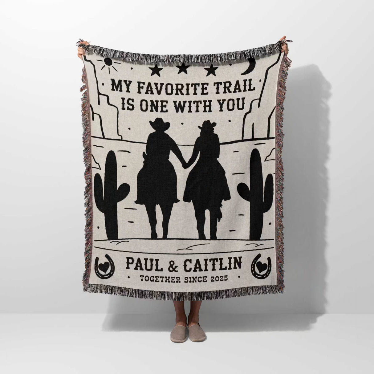 Cowboy and cowgirl on two horses cotton anniversary gift woven throw blanket held by a person with cowboy design and text 'My favorite trail is one with you' by Paul & Caitlin