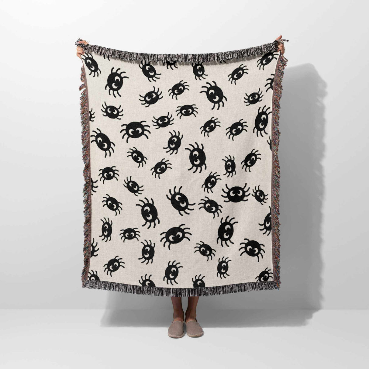 Cute spiders woven throw blanket for halloween décor held by a person on a white background.