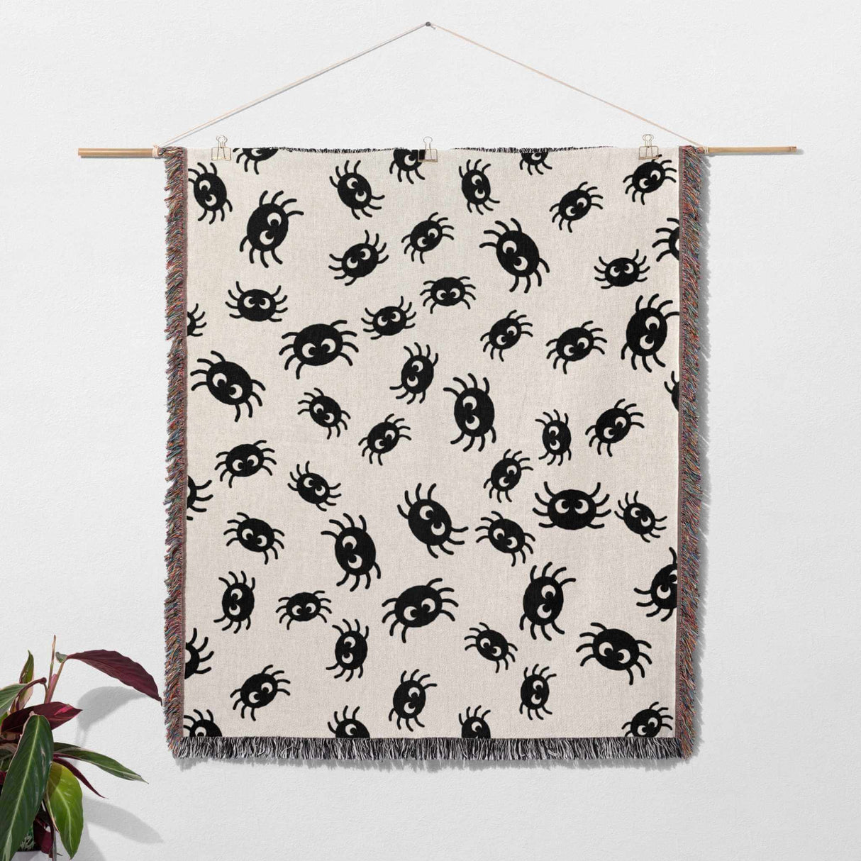 Cute spiders woven throw blanket for Halloween décor on a beige background, hanging against a white wall.