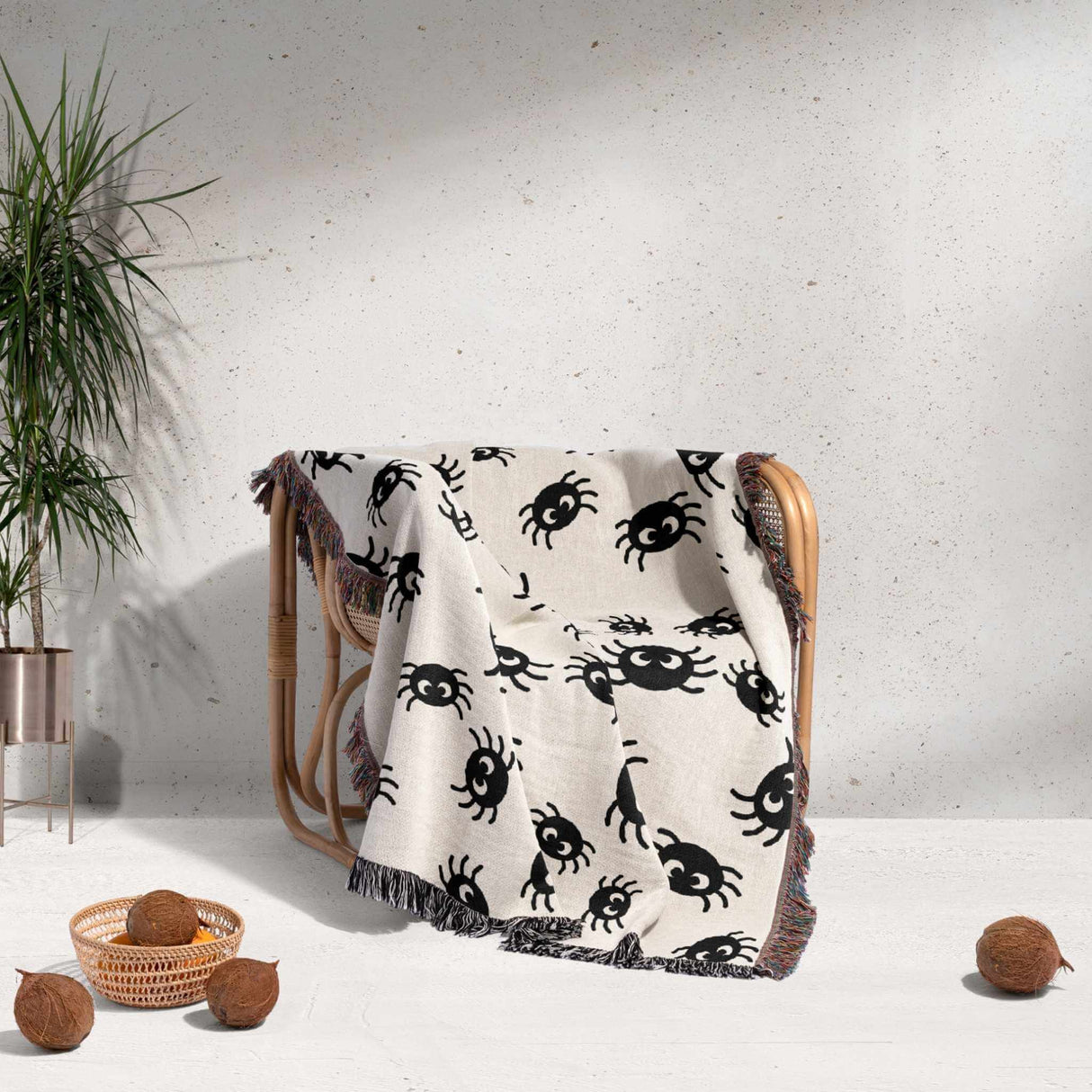 Cute spiders woven throw blanket for Halloween décor draped over a chair against a light gray wall.