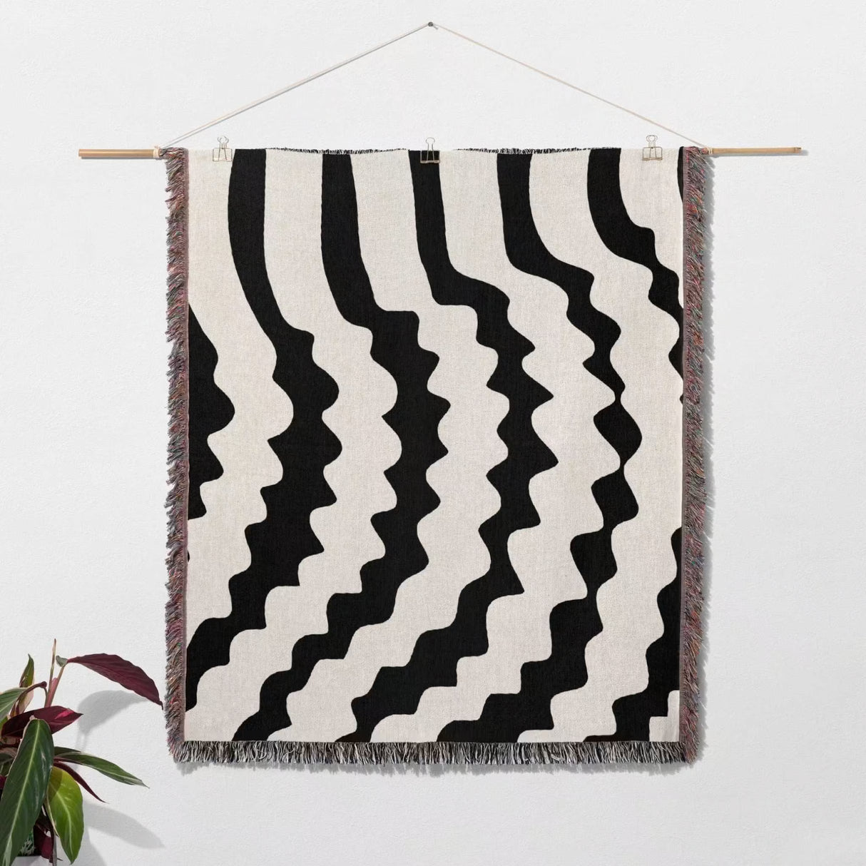 Black and white decorative abstract wavy woven blanket throw hanging on a wall.