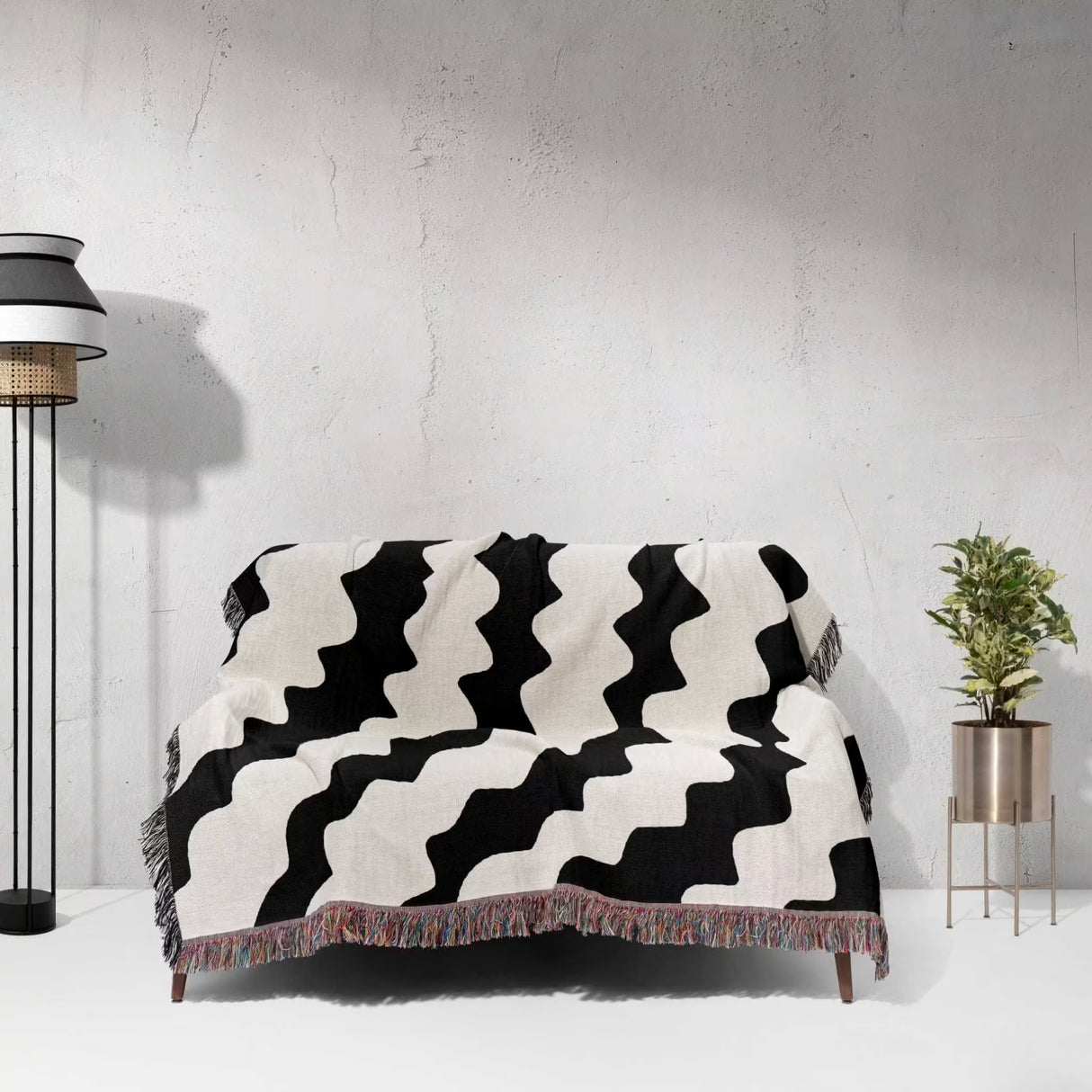 Black and white decorative abstract wavy woven blanket throw draped over a sofa against a light gray wall.