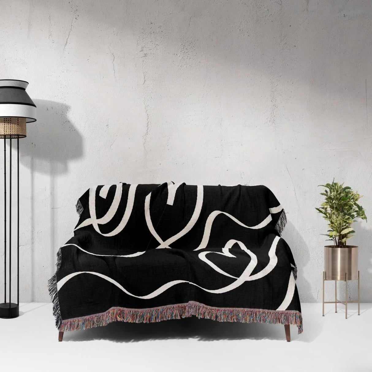 Black and white decorative hearts woven blanket throw draped over a sofa against a light gray wall.