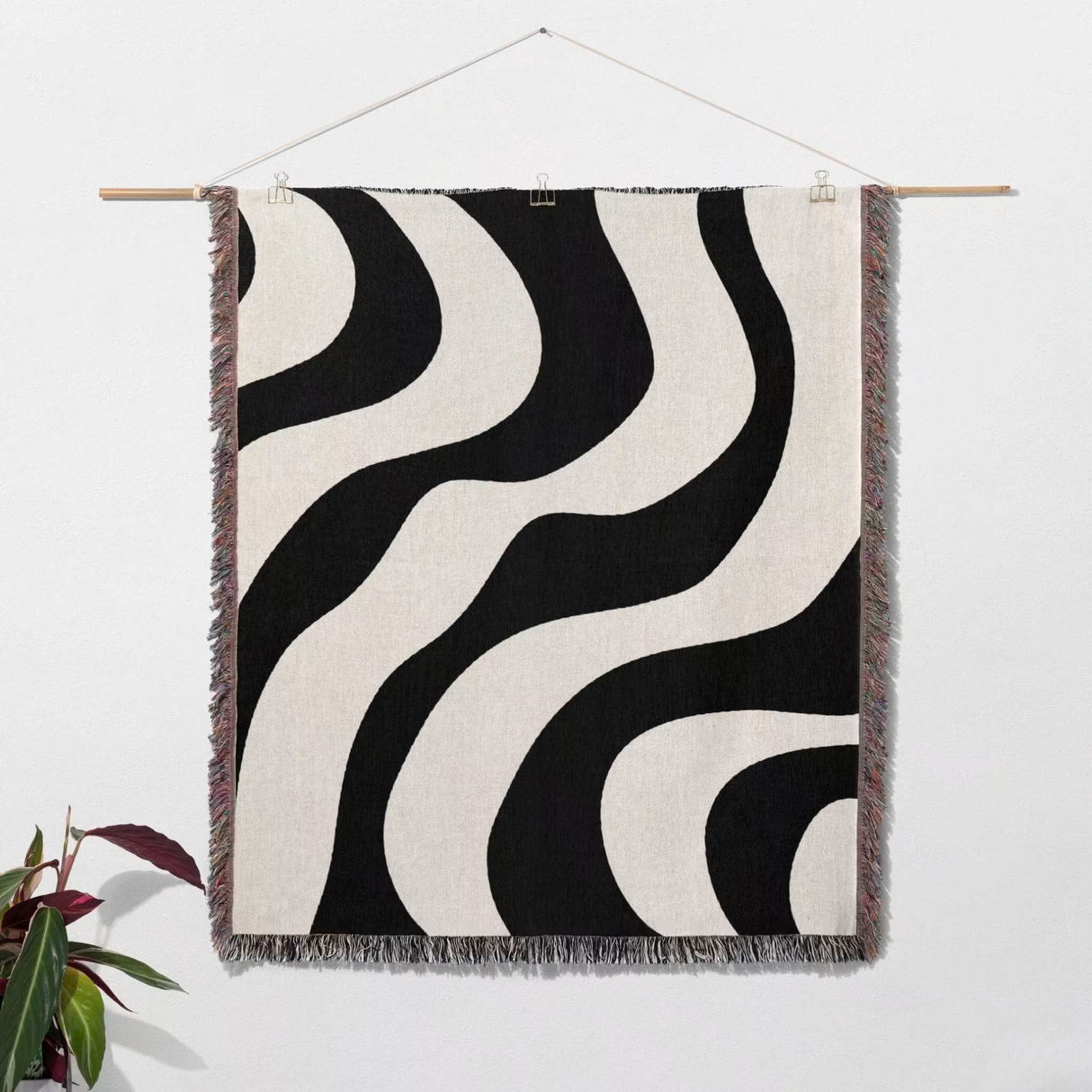 Black and white decorative modern woven blanket throw tapestry hanging on a wooden rod against a white wall.