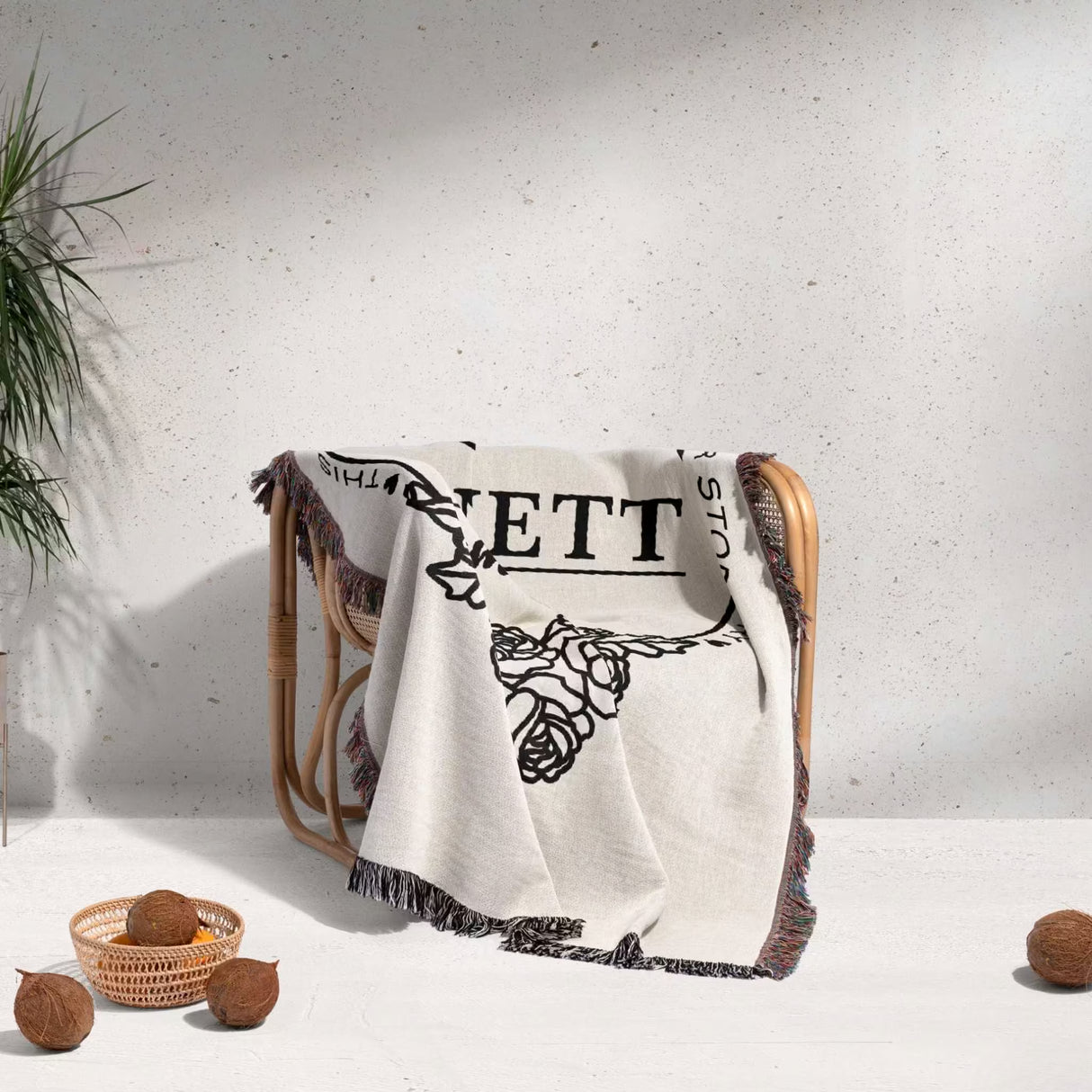 Family name personalized woven throw blanket gift for spouse with floral patterns draped over a chair against a gray wall.