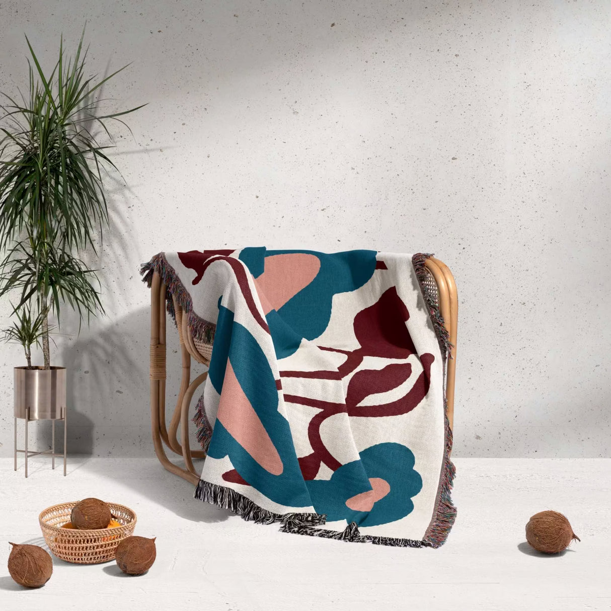 Colorful floral Matisse inspired tapestry throw blanket for couch draped over a chair with a plant and coconuts in the background.