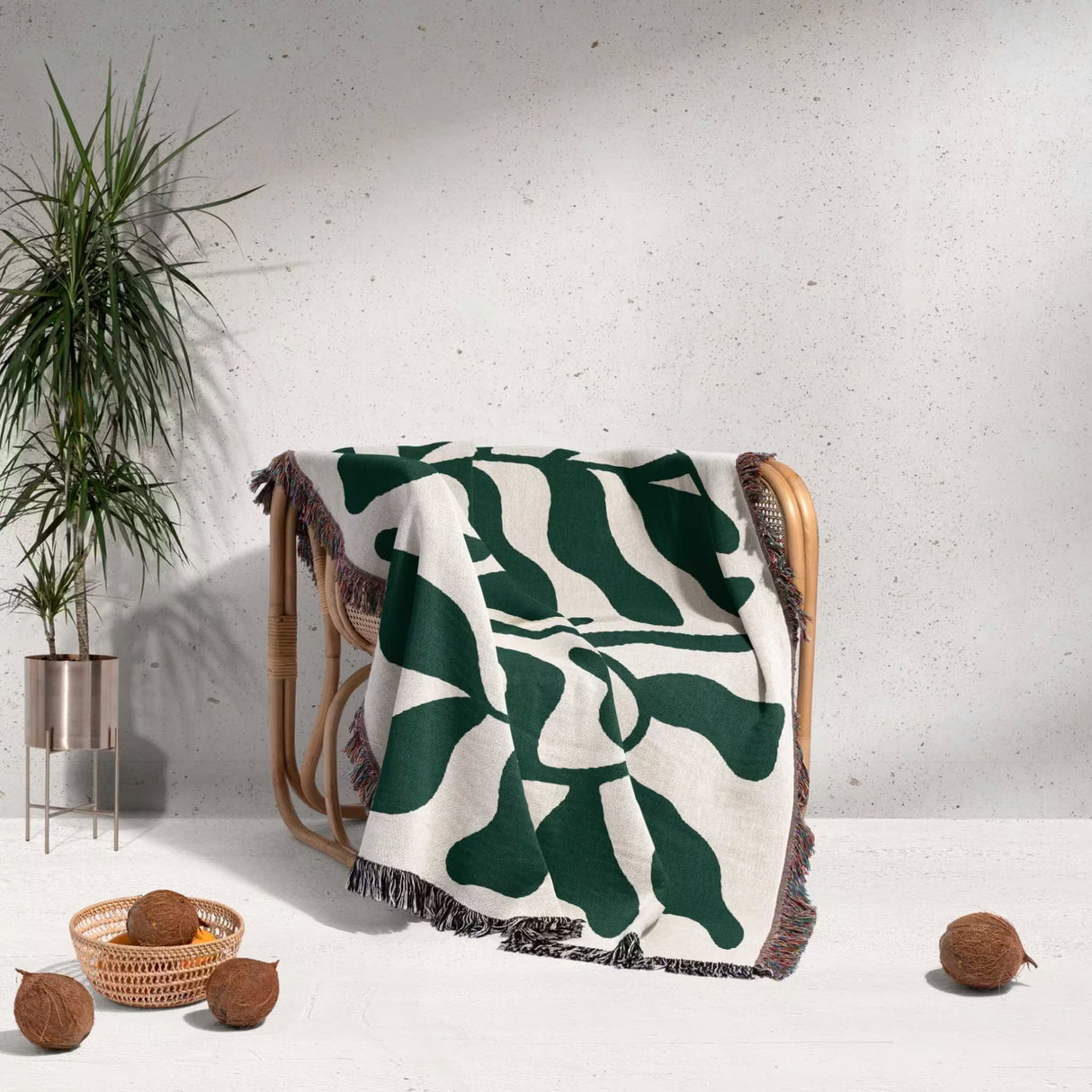 Forest green leaf Matisse throw blanket draped over a wooden chair against a light gray wall.