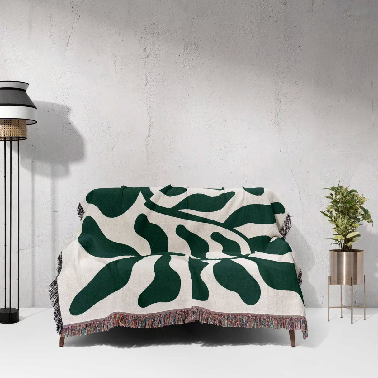 Forest green leaf Matisse throw blanket draped over a chair against a white wall.