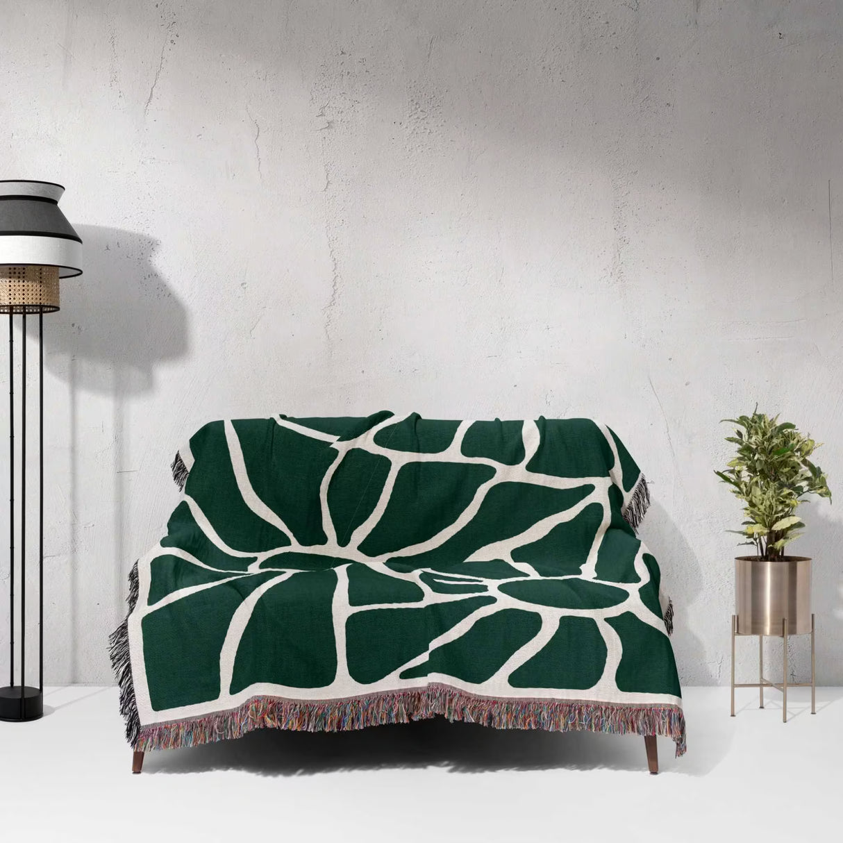 Forest green Matisse tapestry throw blanket for couch draped over a couch against a white wall.