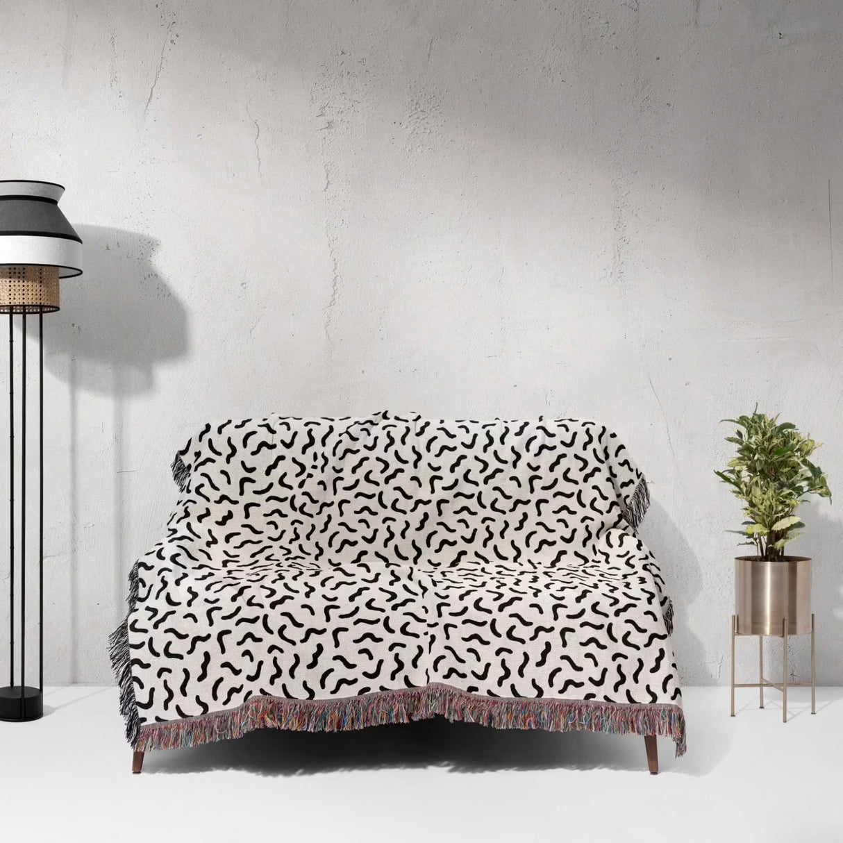Sofa with a black and white funky squiggly woven blanket throw tapestry against a white wall.