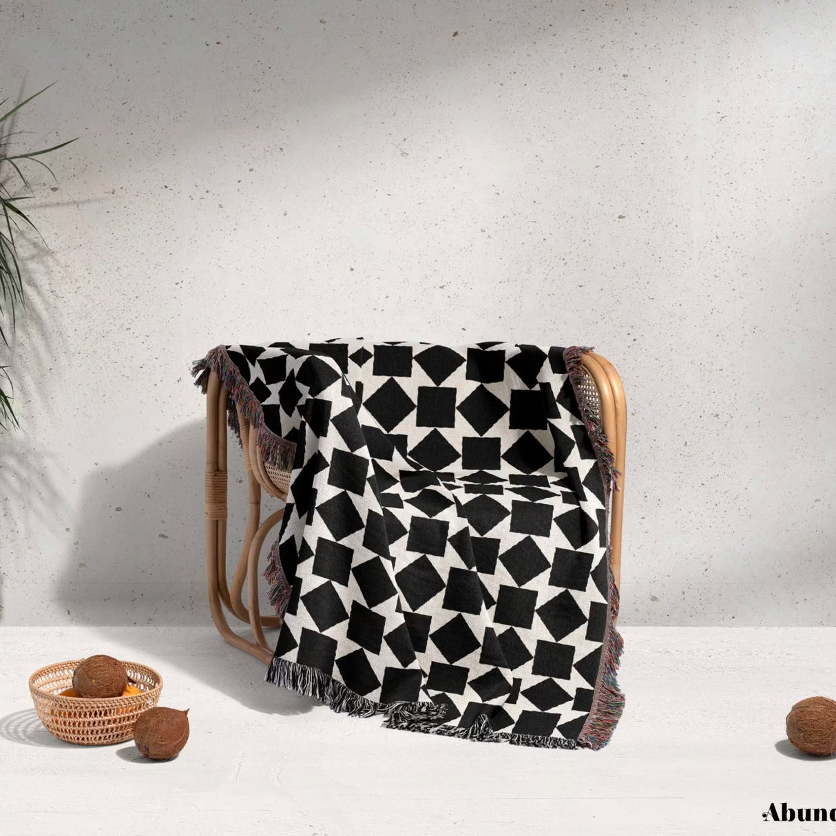 Black and white geometric square patterned woven blanket throw draped over a wooden chair against a light background.