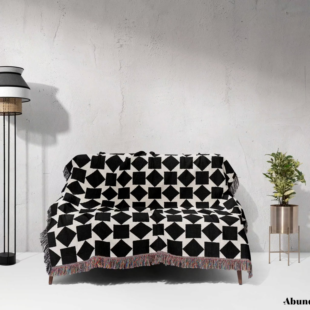 Black and white geometric square patterned woven blanket throw draped over a sofa against a white wall.