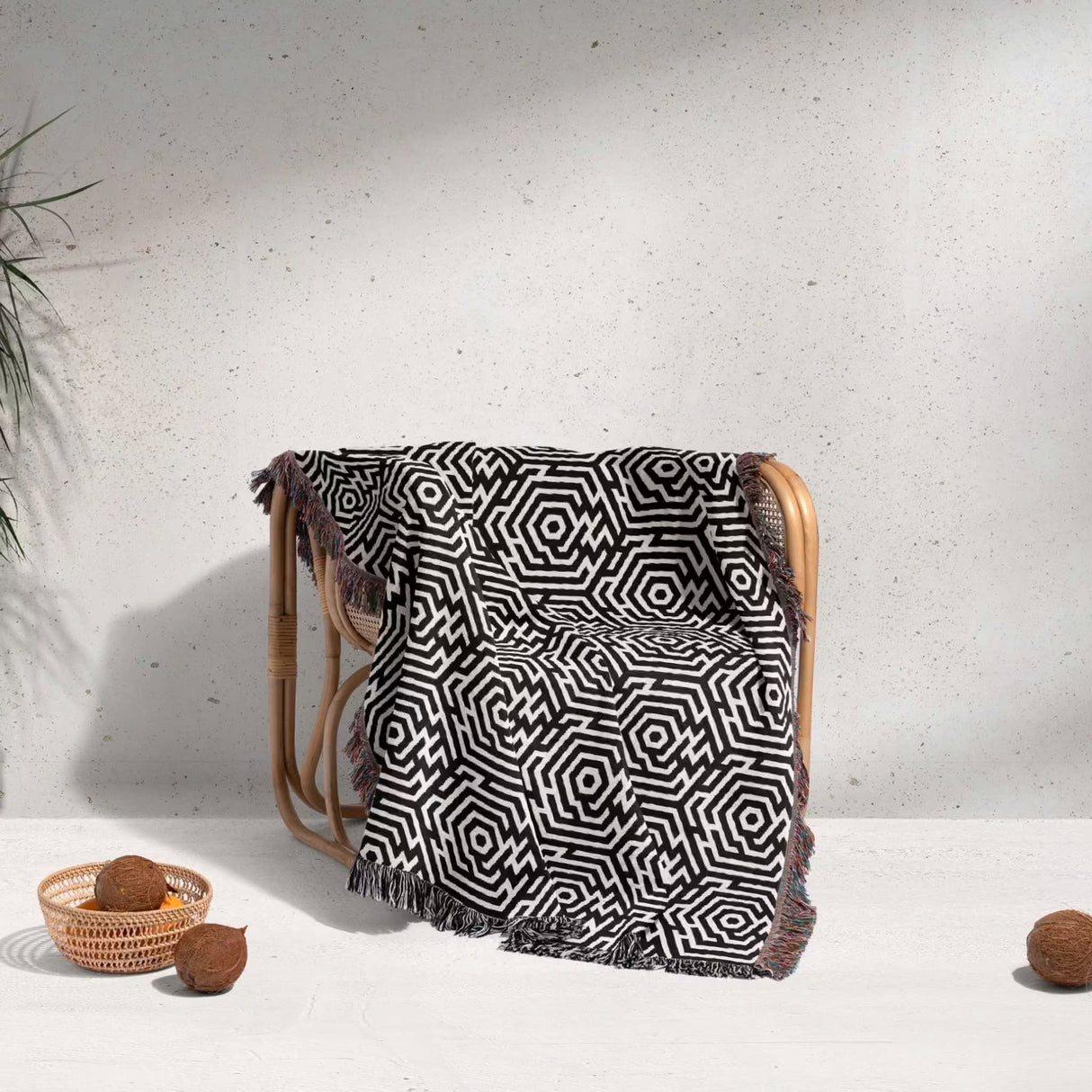 Black and white labyrinth hexagon pattern woven blanket throw cover ing a wooden chair against a white wall.