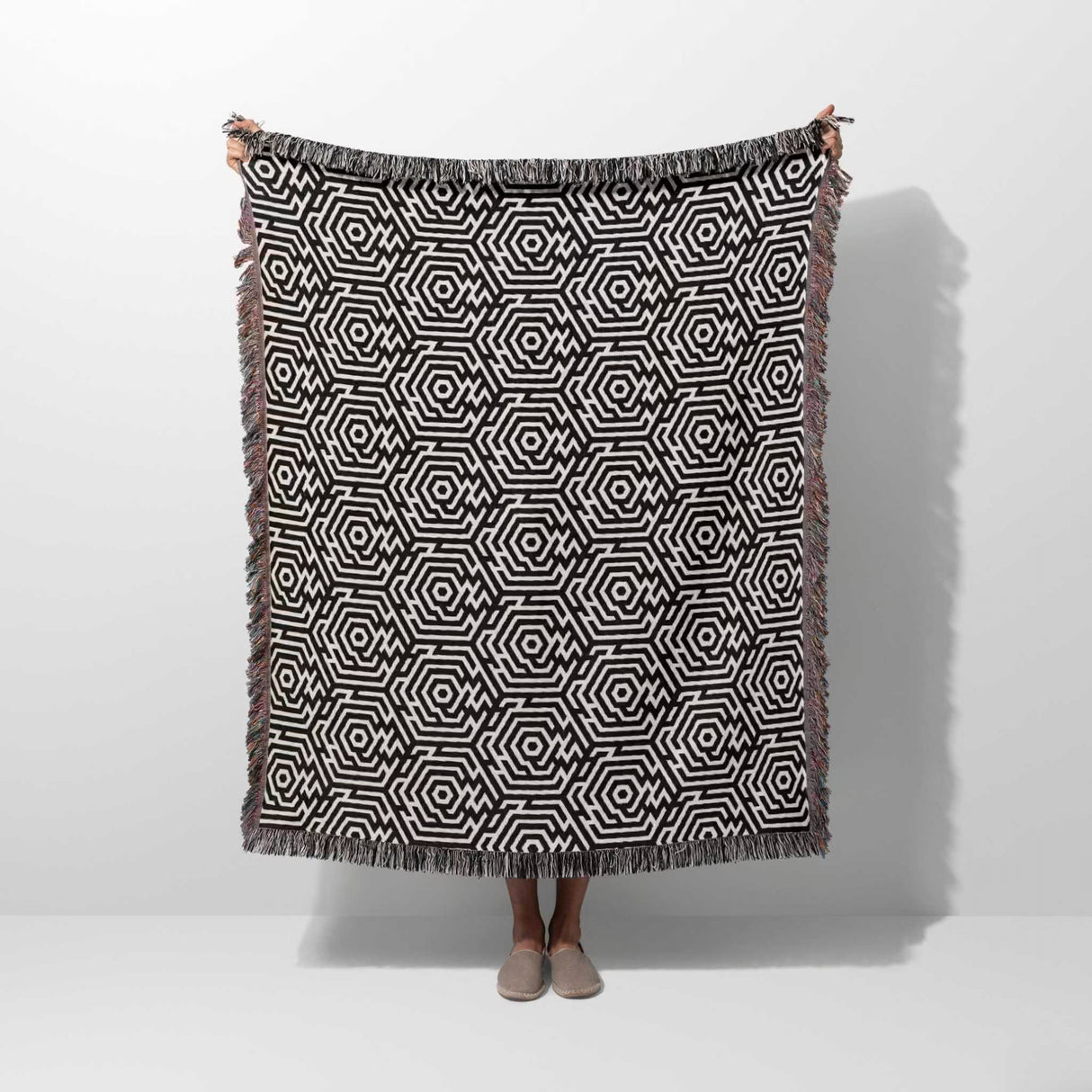 Black and white labyrinth hexagon pattern woven blanket throw held by a person on a white background.