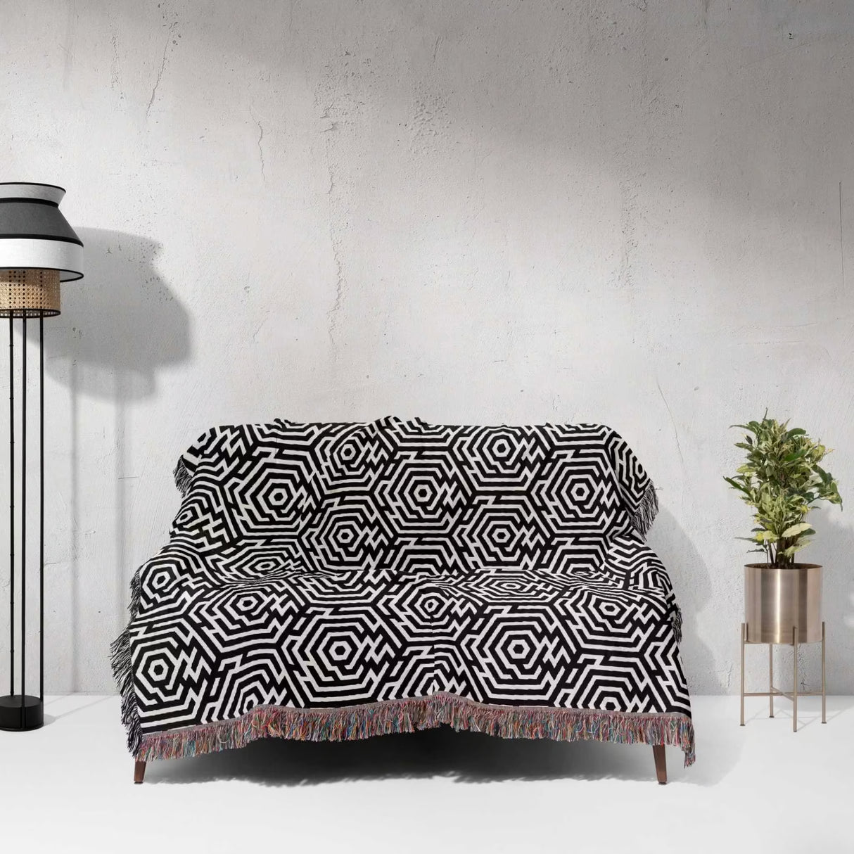Black and white labyrinth hexagon pattern woven blanket throw on a sofa against a white wall.