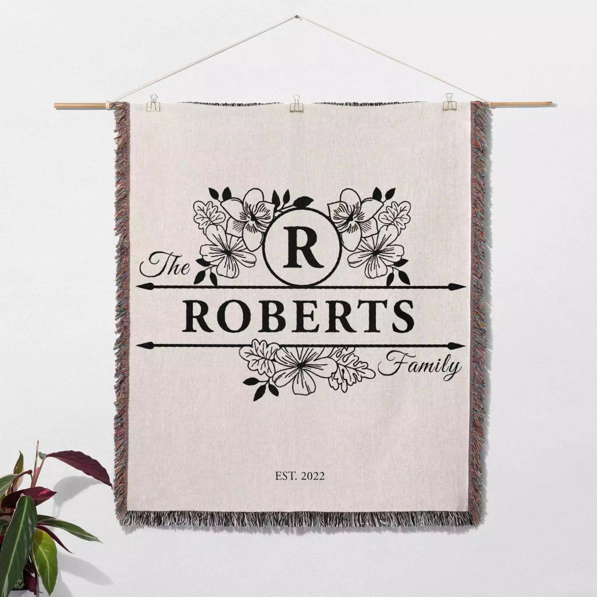 Personalized last name monogram blanket with 'The Roberts Family' design on a white wall.