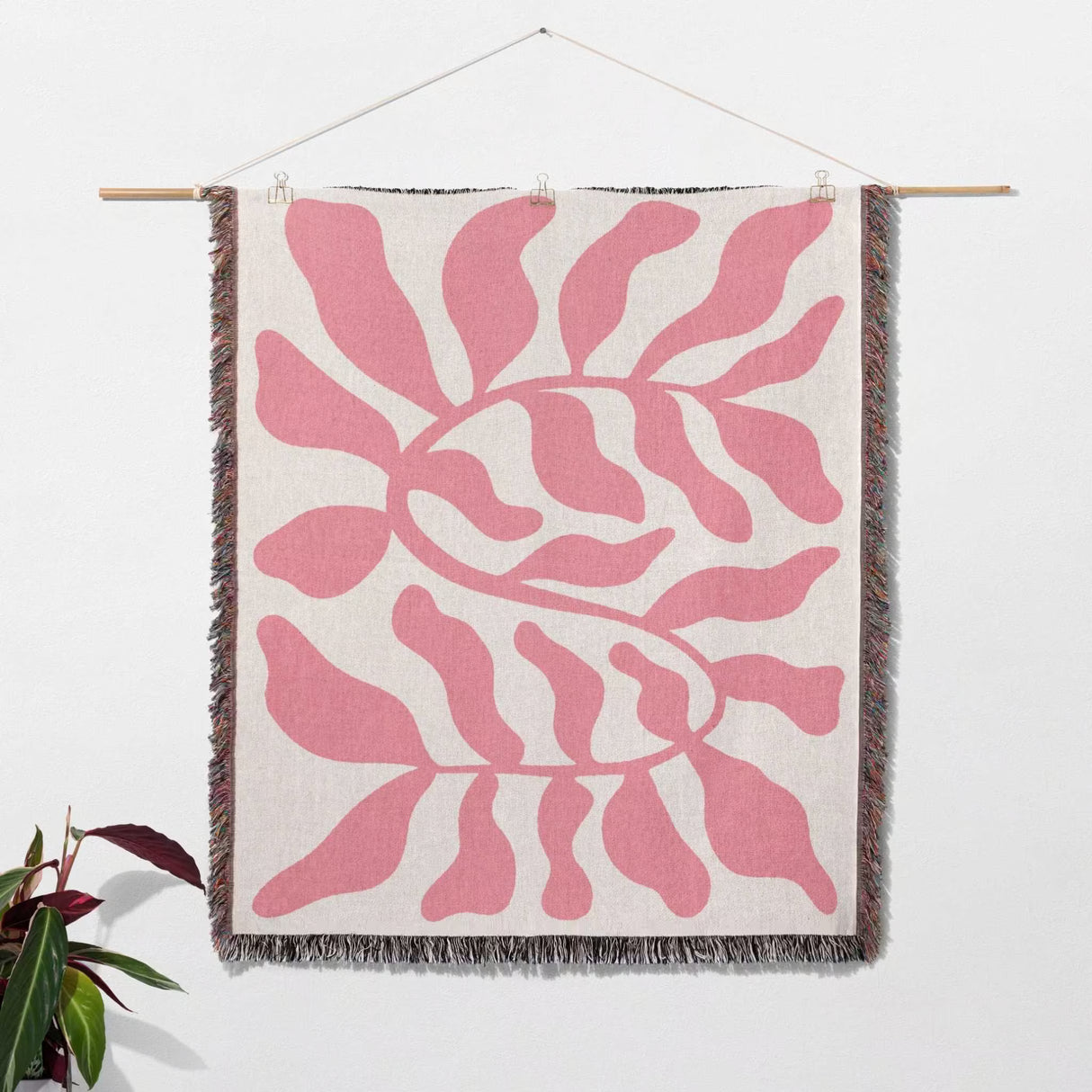 Lighter red leaf Matisse throw blanket hanging on a wooden rod against a white wall.