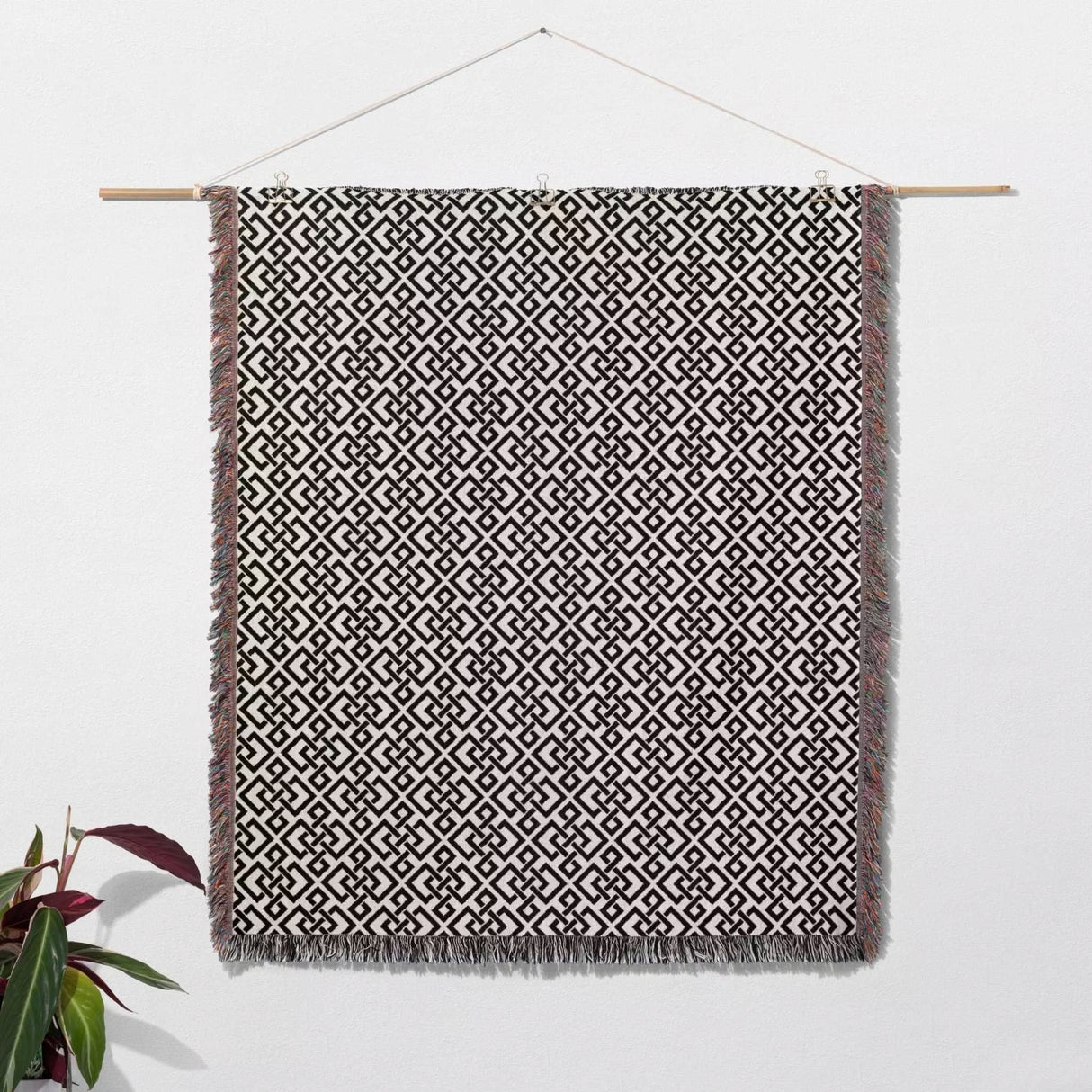 Black and white luxury geometric patterned woven blanket throw tapestry with hanging on a wooden rod against a white wall.